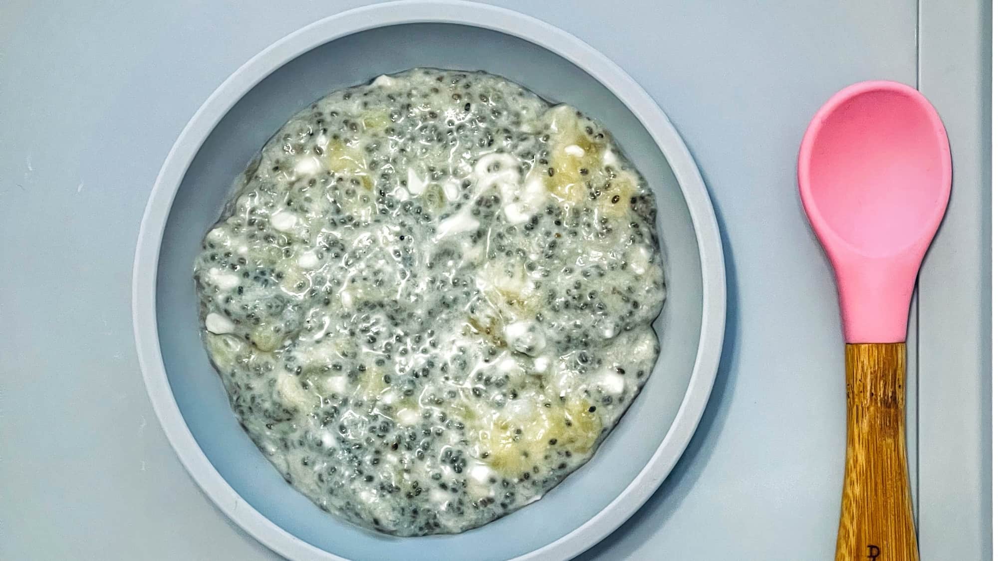 Image of banana chia pudding in a blue bowl with a pink spoon.