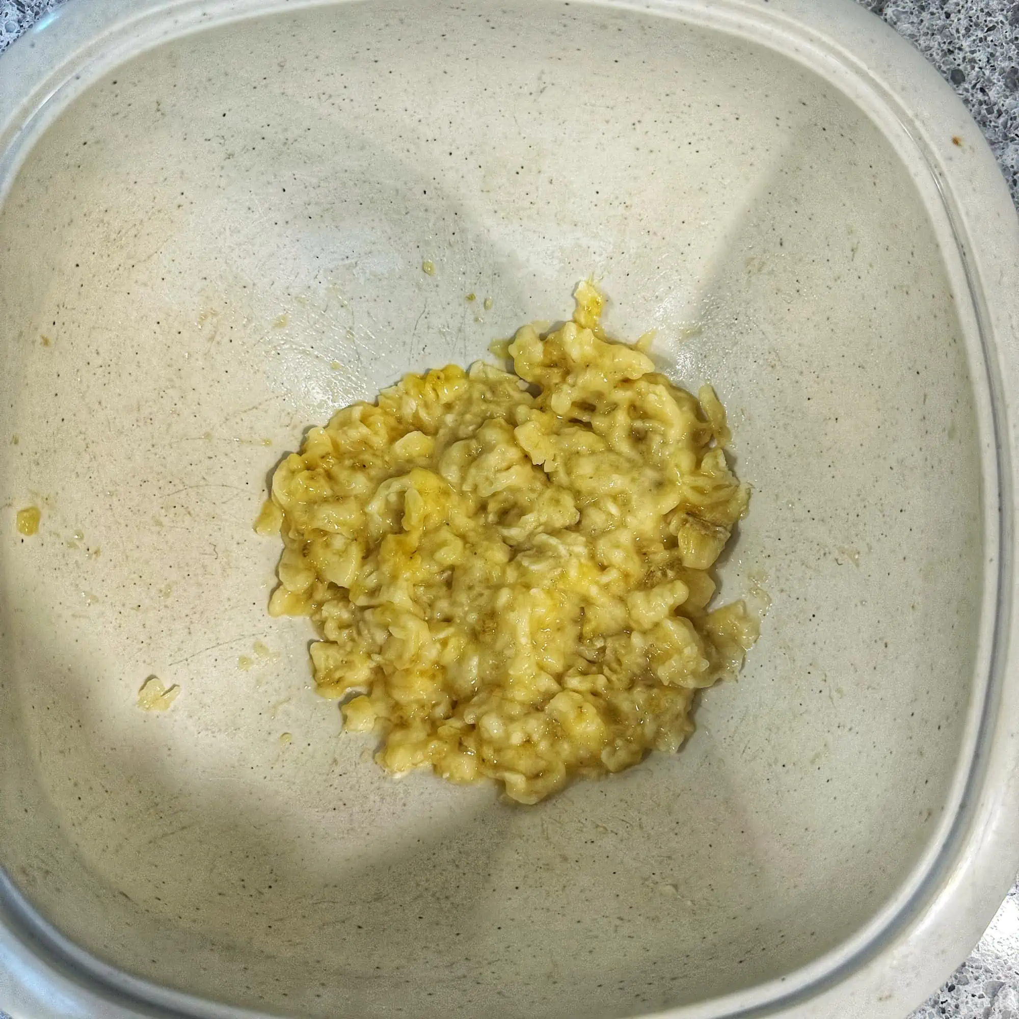 Image of the first step of the recipe for ABC muffins, mashing the banana in a white bowl.