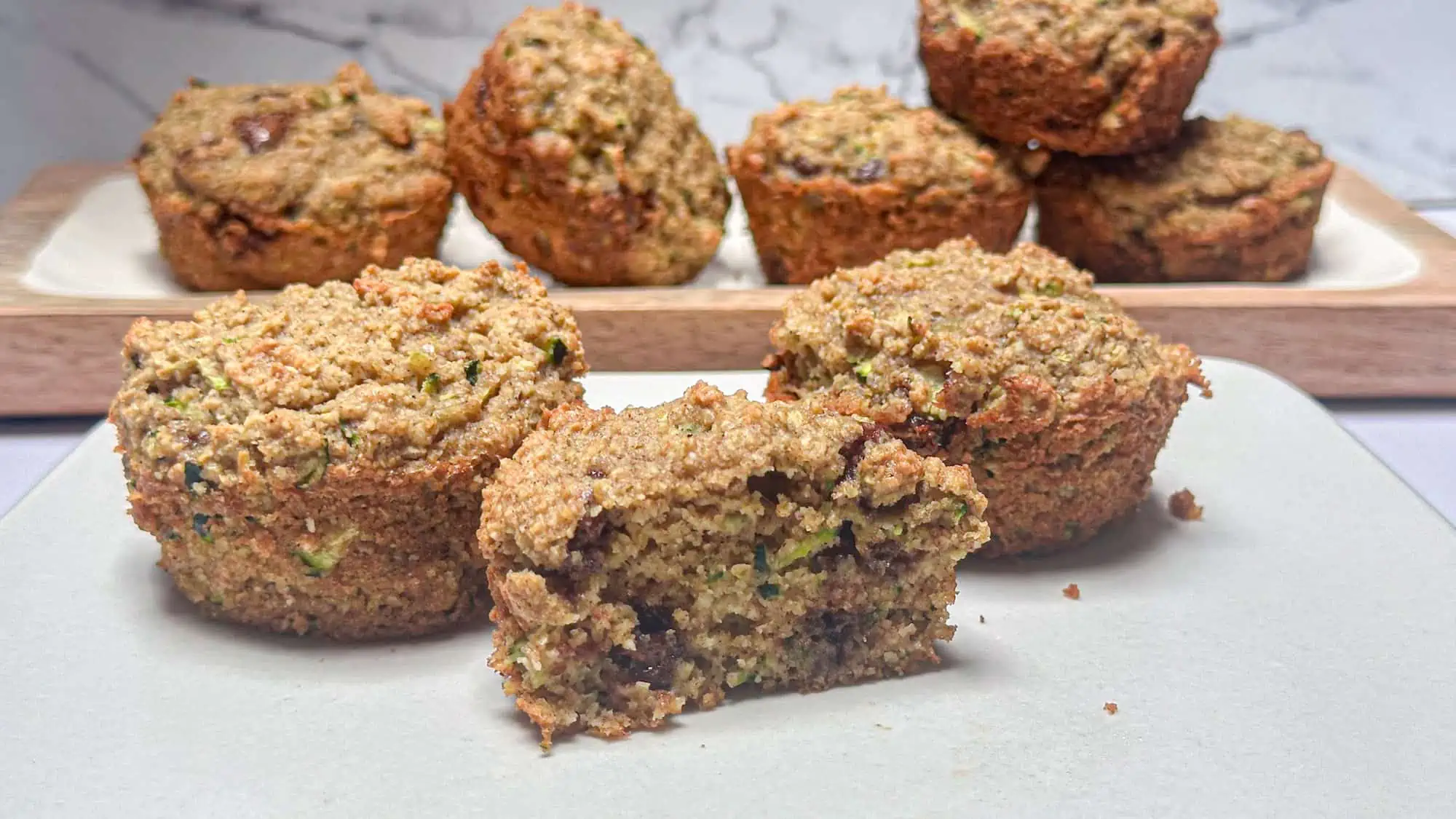 Almond flour zucchini muffins on white plate and some muffins stacked on white wooden plate with white marble backdrop.