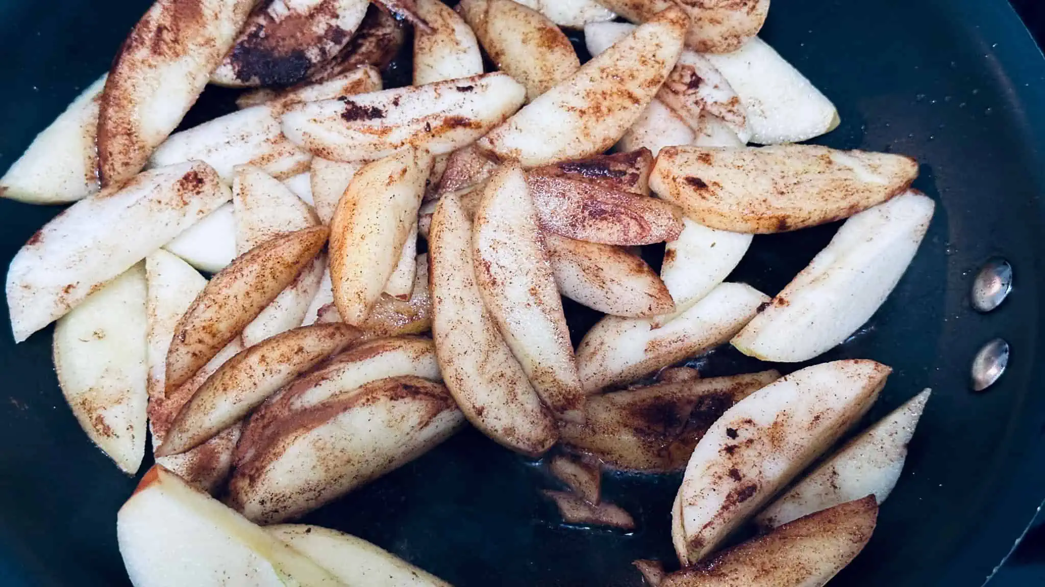 Step 3 of cinnamon apples. Adding cinnamon and vanilla to apple slices in non stick pan.