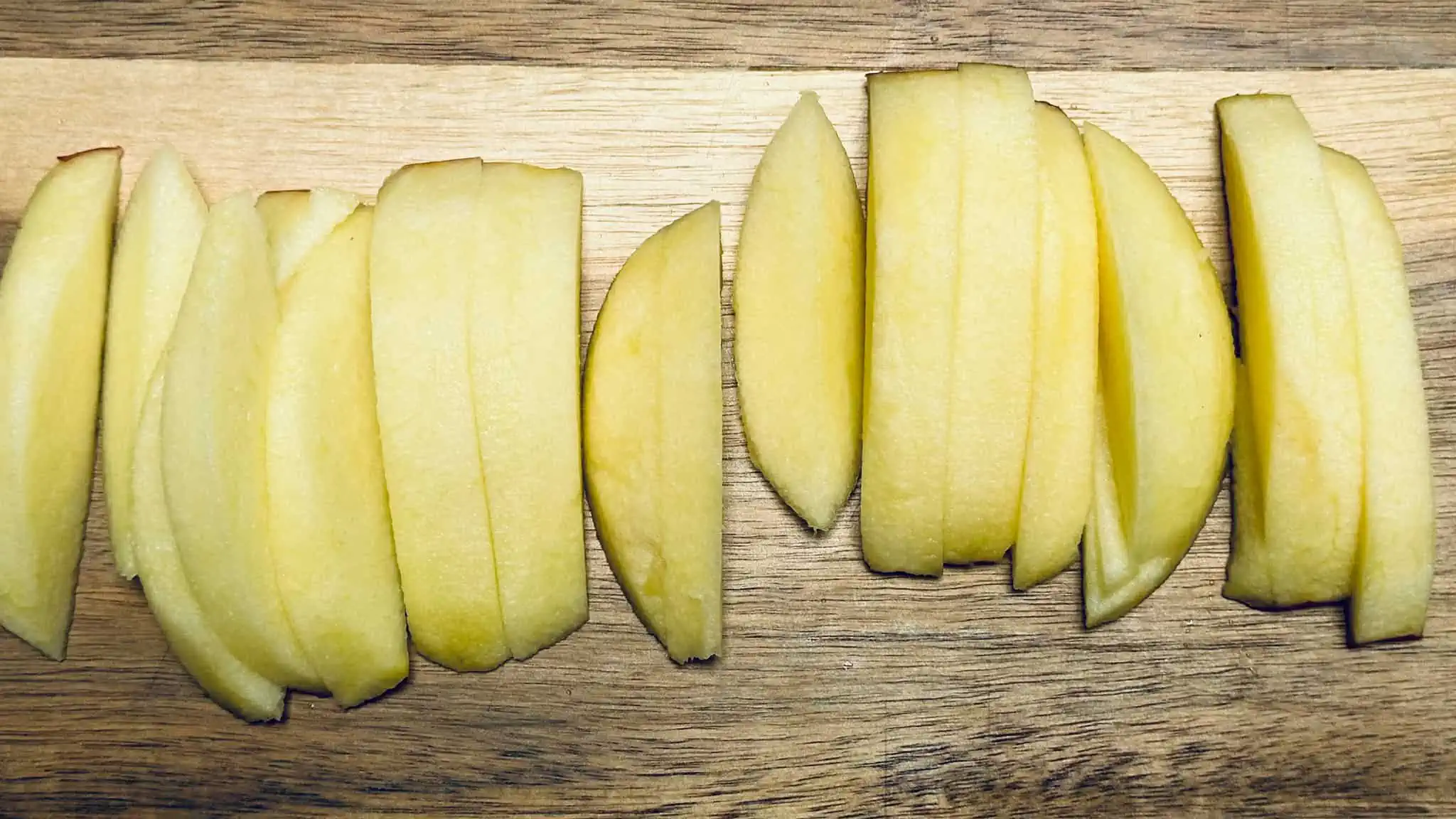 Image of step 1 for cinnamon apples. Apples are peeled and sliced on wood cutting board.