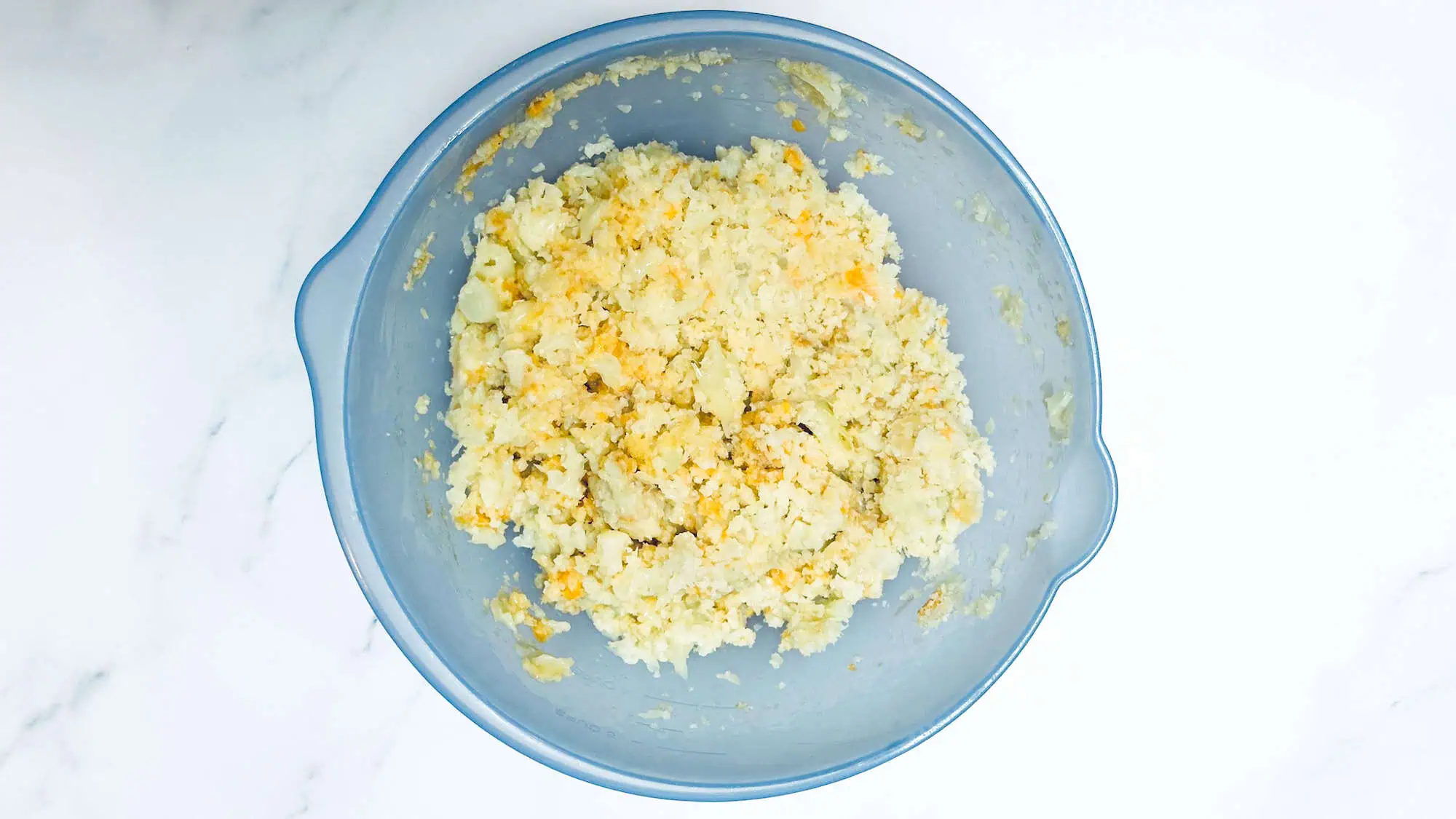 Step 2 for cauliflower tater tots - adding all ingredients to a blue bowl and stir to combine.