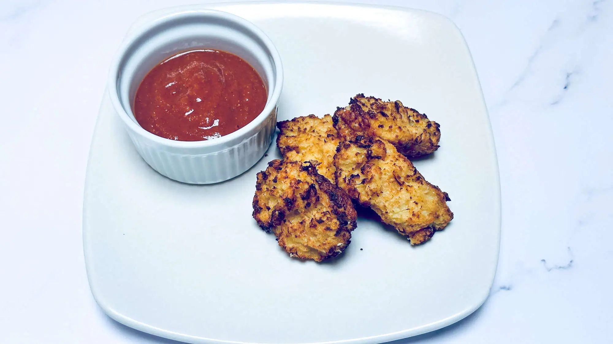 Cauliflower tater tots on white plate with barbecue dipping sauce.