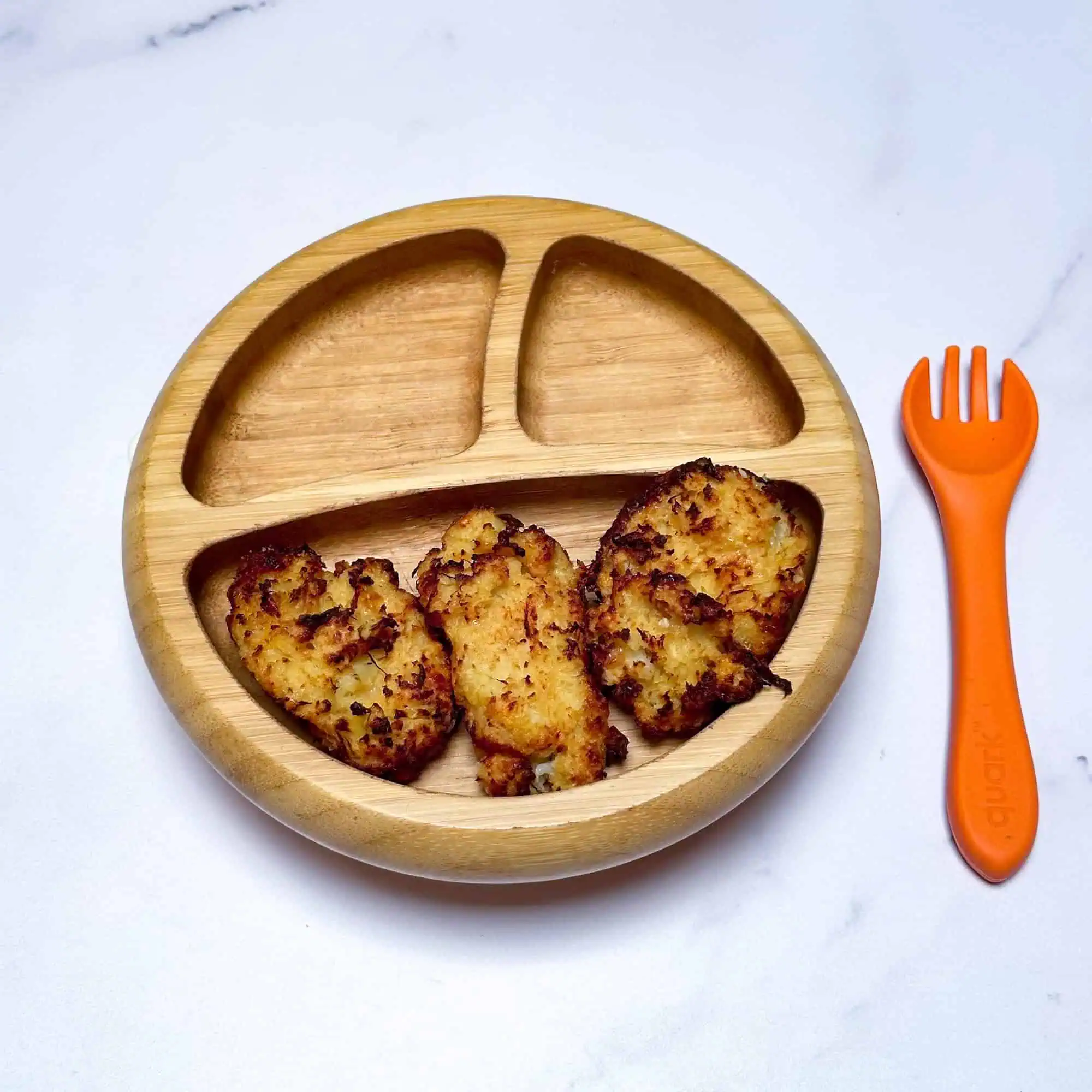 Cauliflower tater tots in wooden toddler bowl with orange fork.