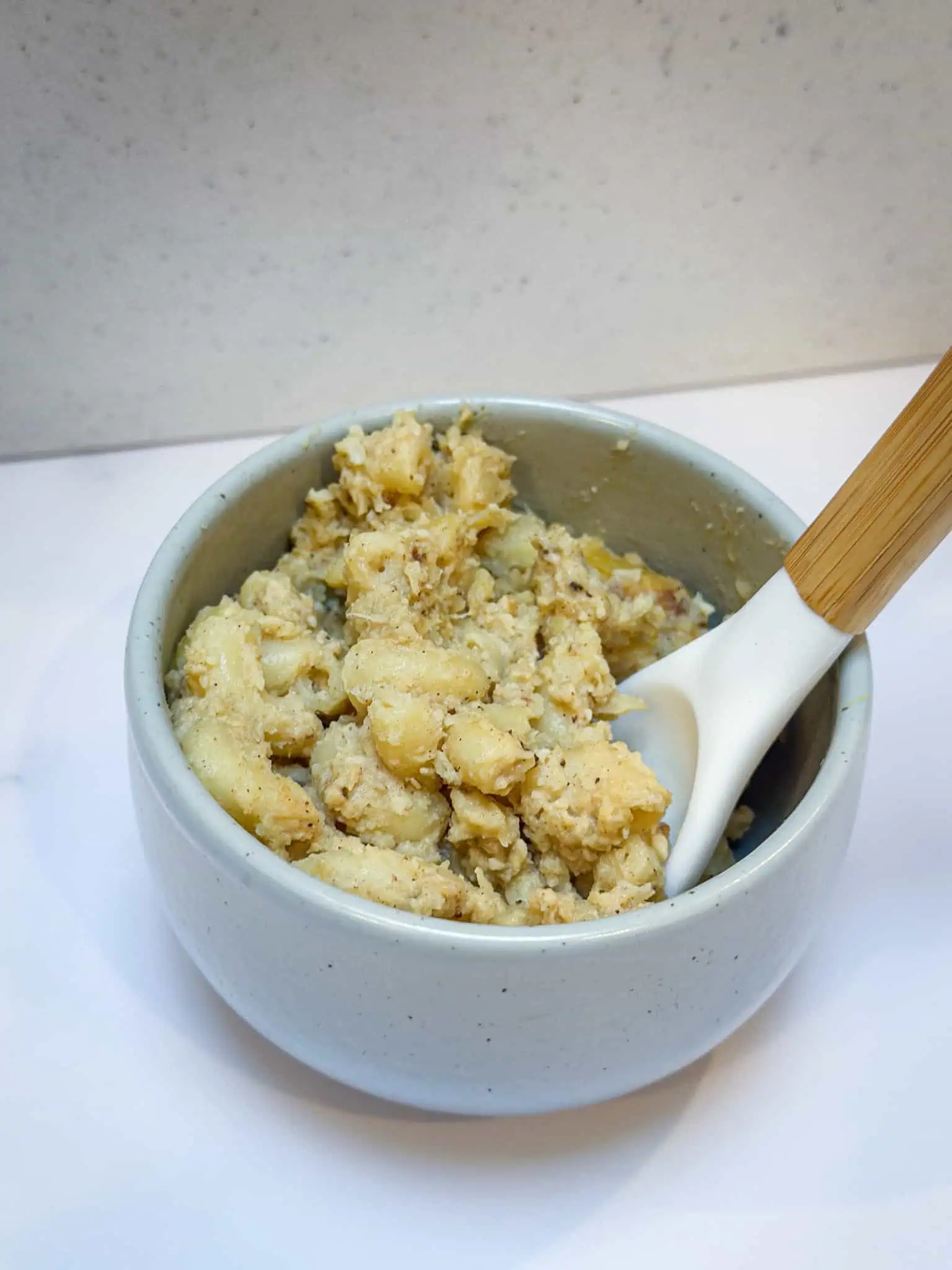 Dairy-free mac and cheese in small bowl on white marble background with wooden spoon.