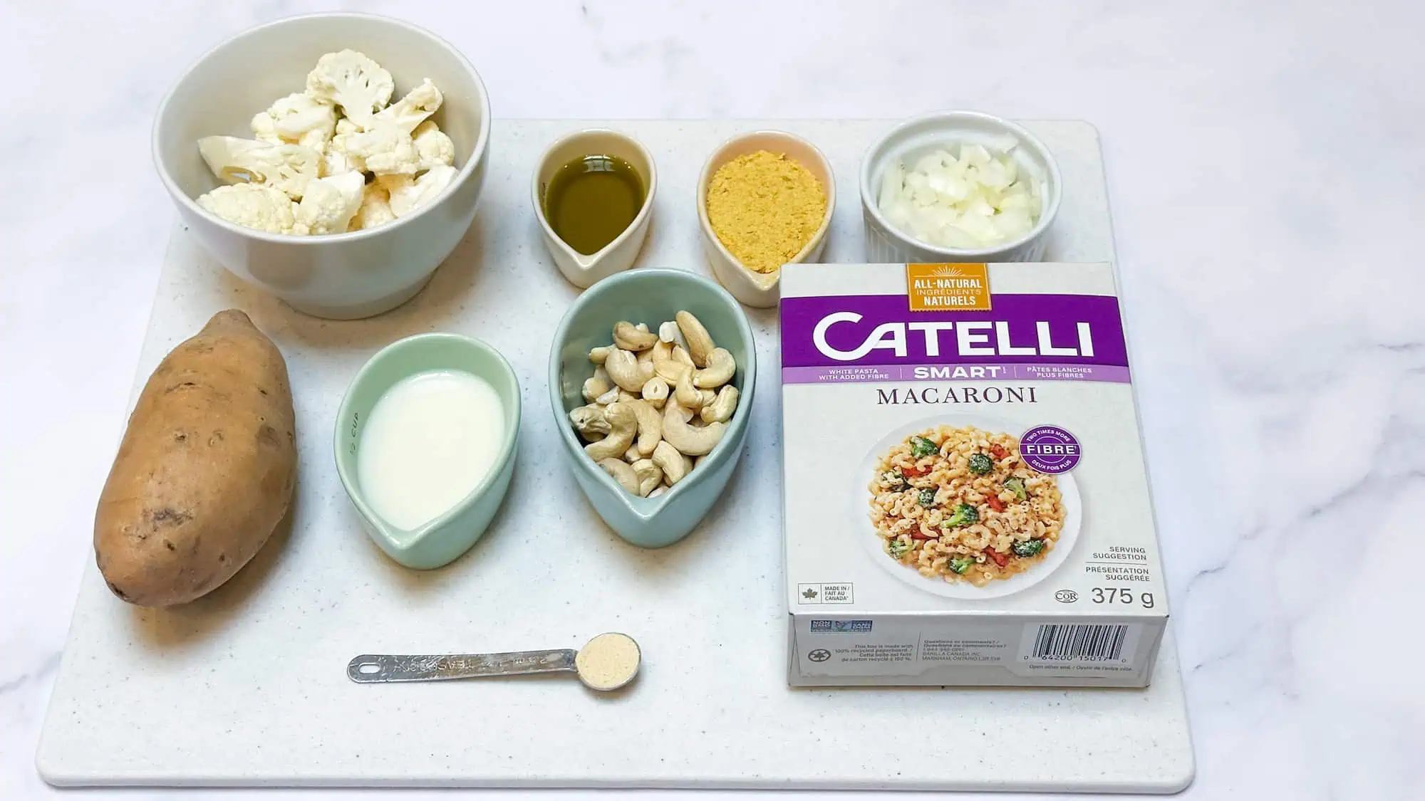 Ingredients for dairy-free mac and cheese on white cutting board on white marble backdrop.