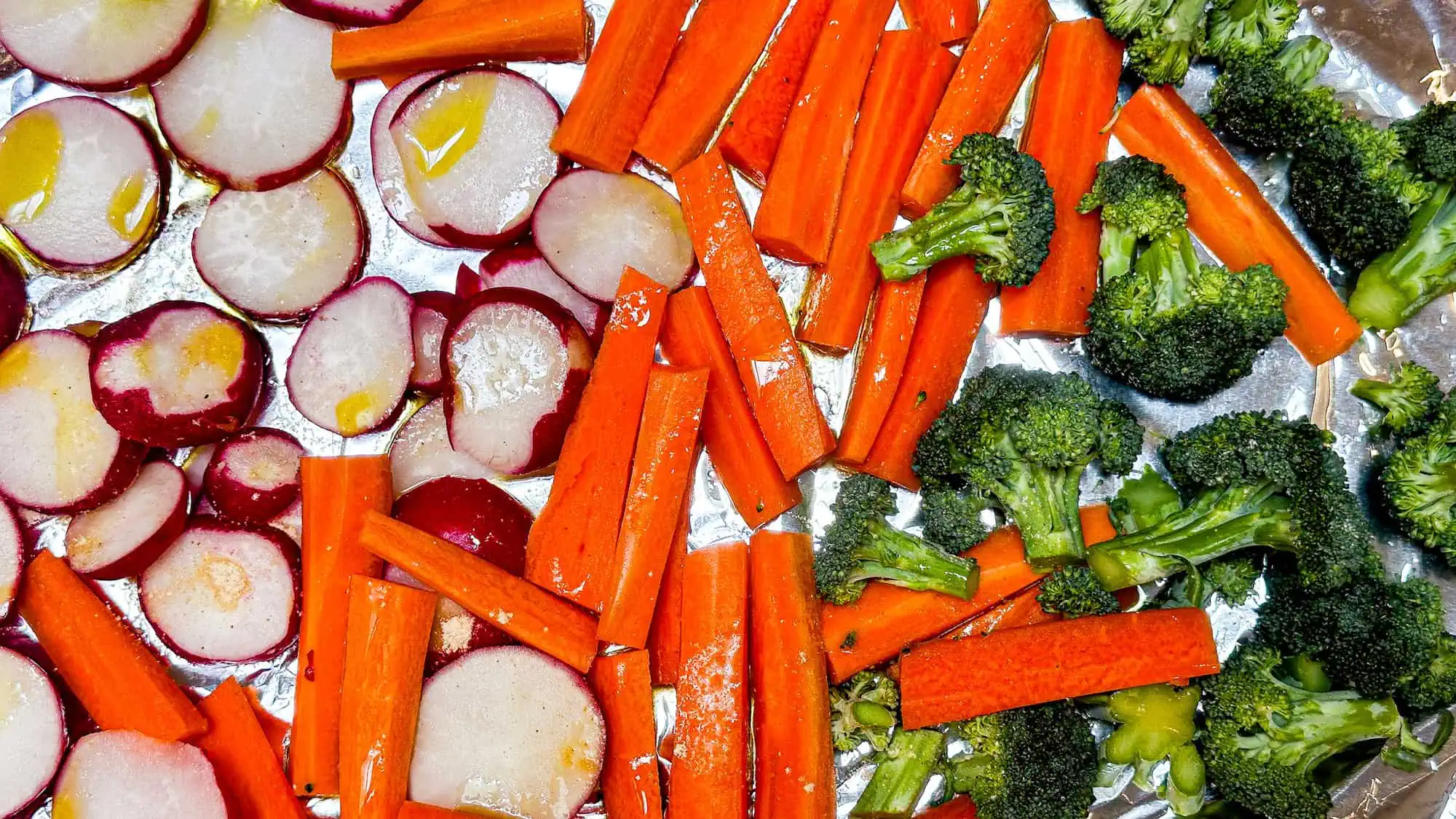 Step 2 for roasted vegetables. Roasted vegetables added to baking sheet drizzled with olive oil.