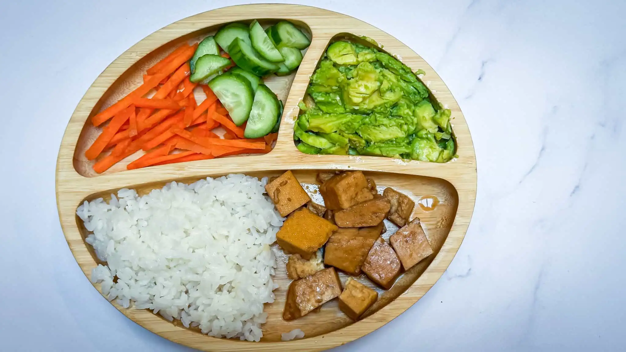 Tofu rice bowls, deconstructed onto a toddler wooden plate on white marble backdrop.