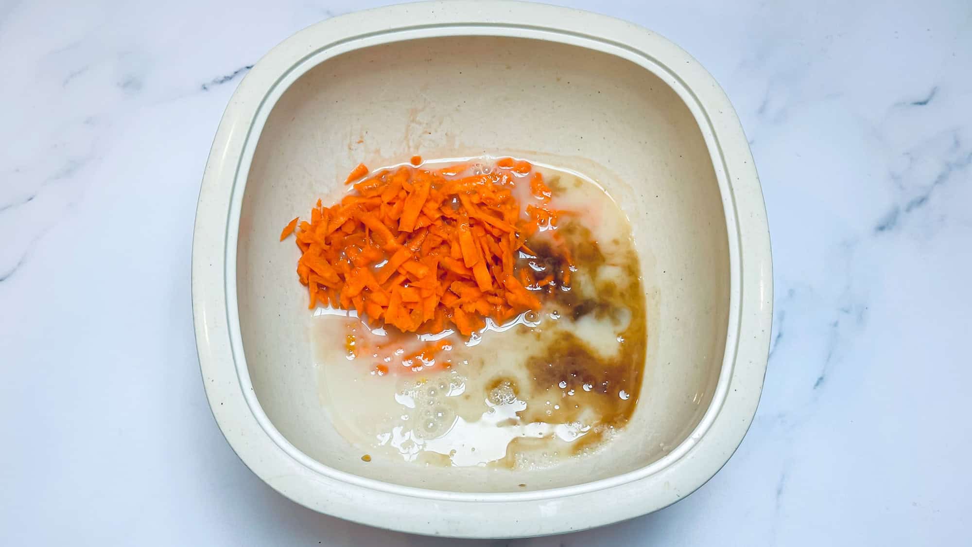 Wet ingredients for carrot cake oatmeal added to white plastic bowl.