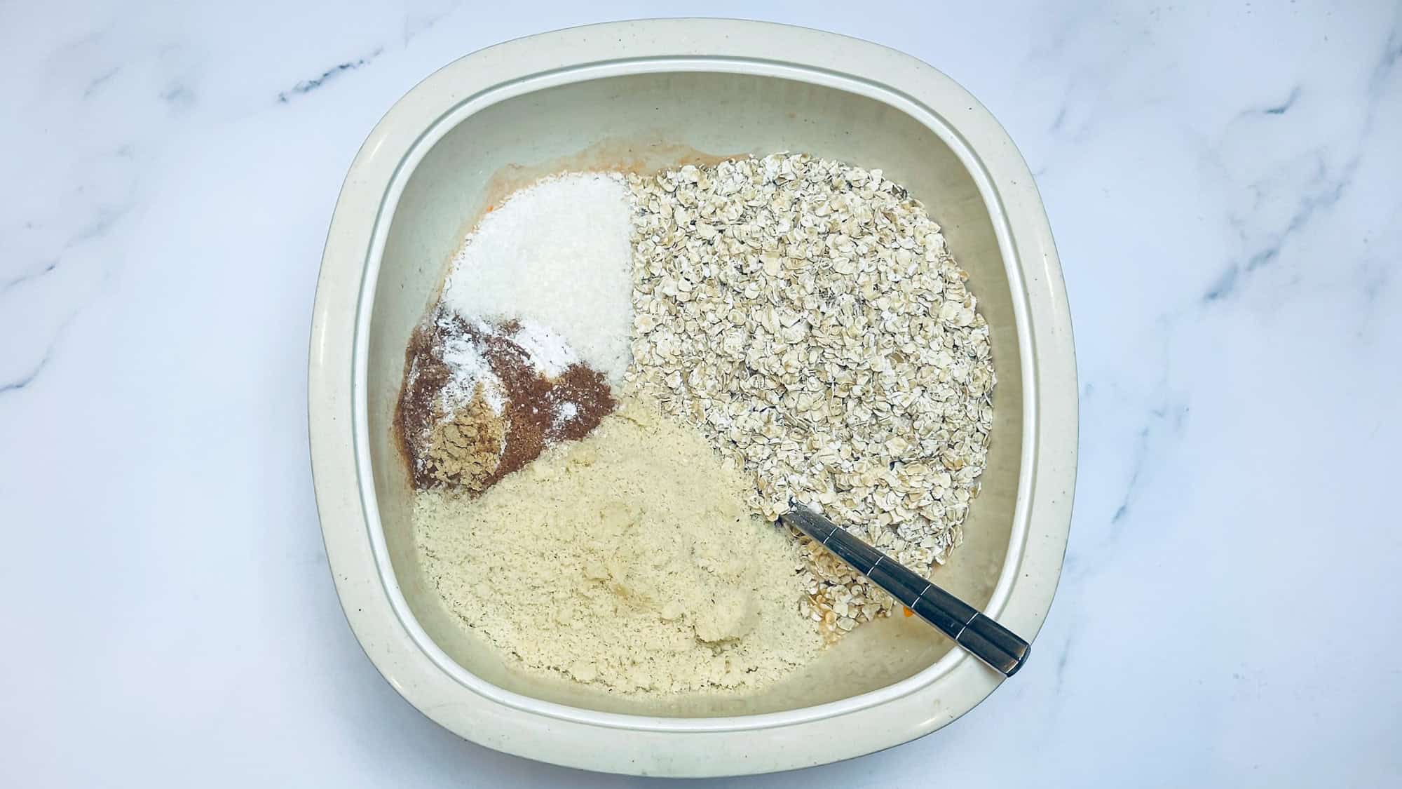 Step 2 for baked carrot cake oatmeal. Adding dry ingredients to wet ingredients in white bowl.