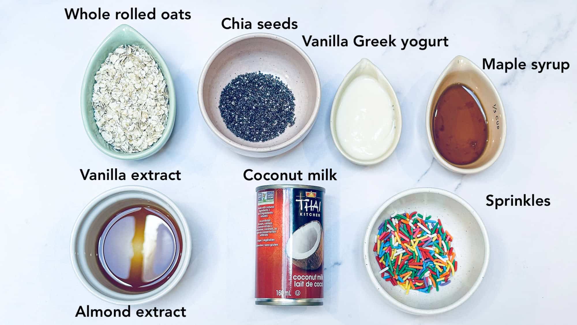 Ingredients for overnight oats labelled and on white marble background.