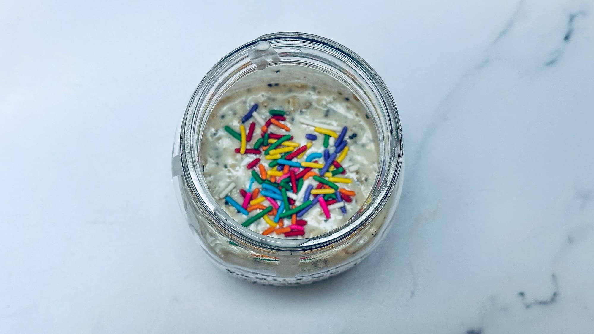 Ingredients for overnight oats added to glass mason jar with visible sprinkles on top.