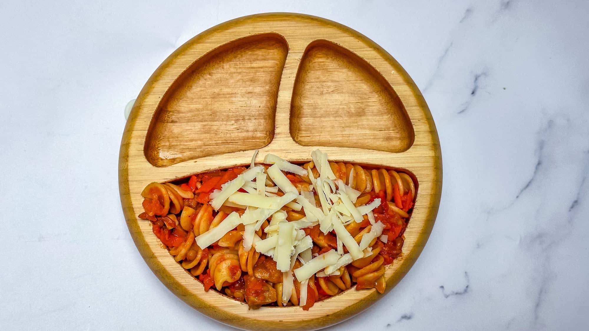 Lentil pasta in wooden toddler bowl with grated parmesan cheese on top