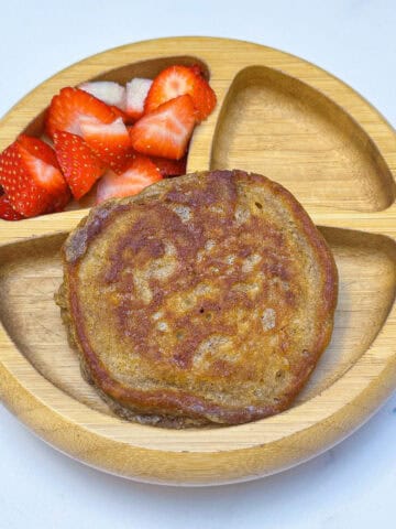 Image of mini pancake served with strawberries in wooden toddler bowl on white marble backdrop.