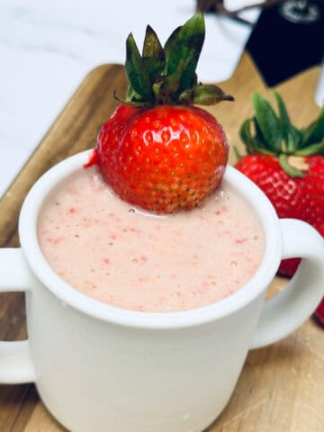 Strawberry peanut butter smoothie in white silicone toddler cup on wooden cutting board with whole strawberries in background.