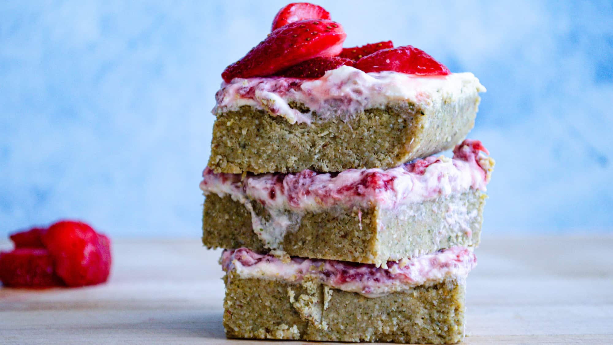 Strawberry yogurt bars stacked on top of one another with blue background and on wooden board.