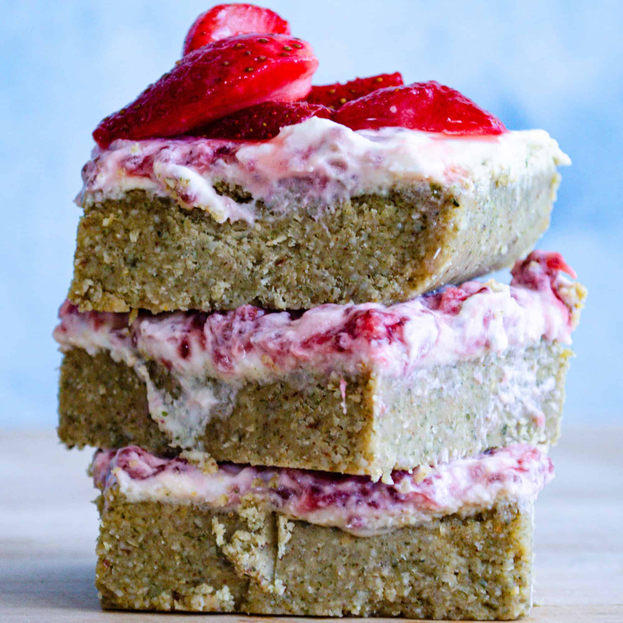 Strawberry yogurt bars stacked on top of one another with blue background and on wooden board.