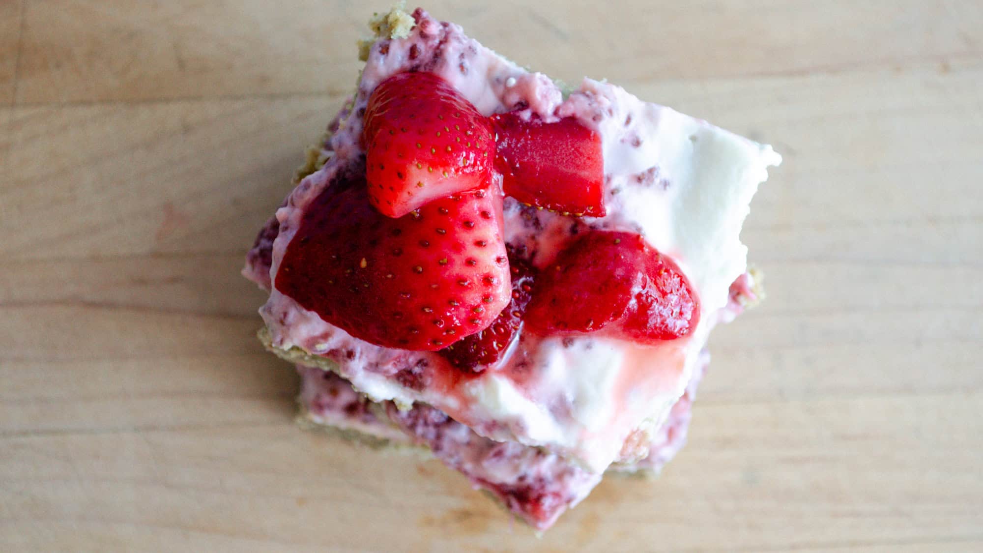 Top down photo of strawberry yogurt bar with strawberries on top on wooden board.