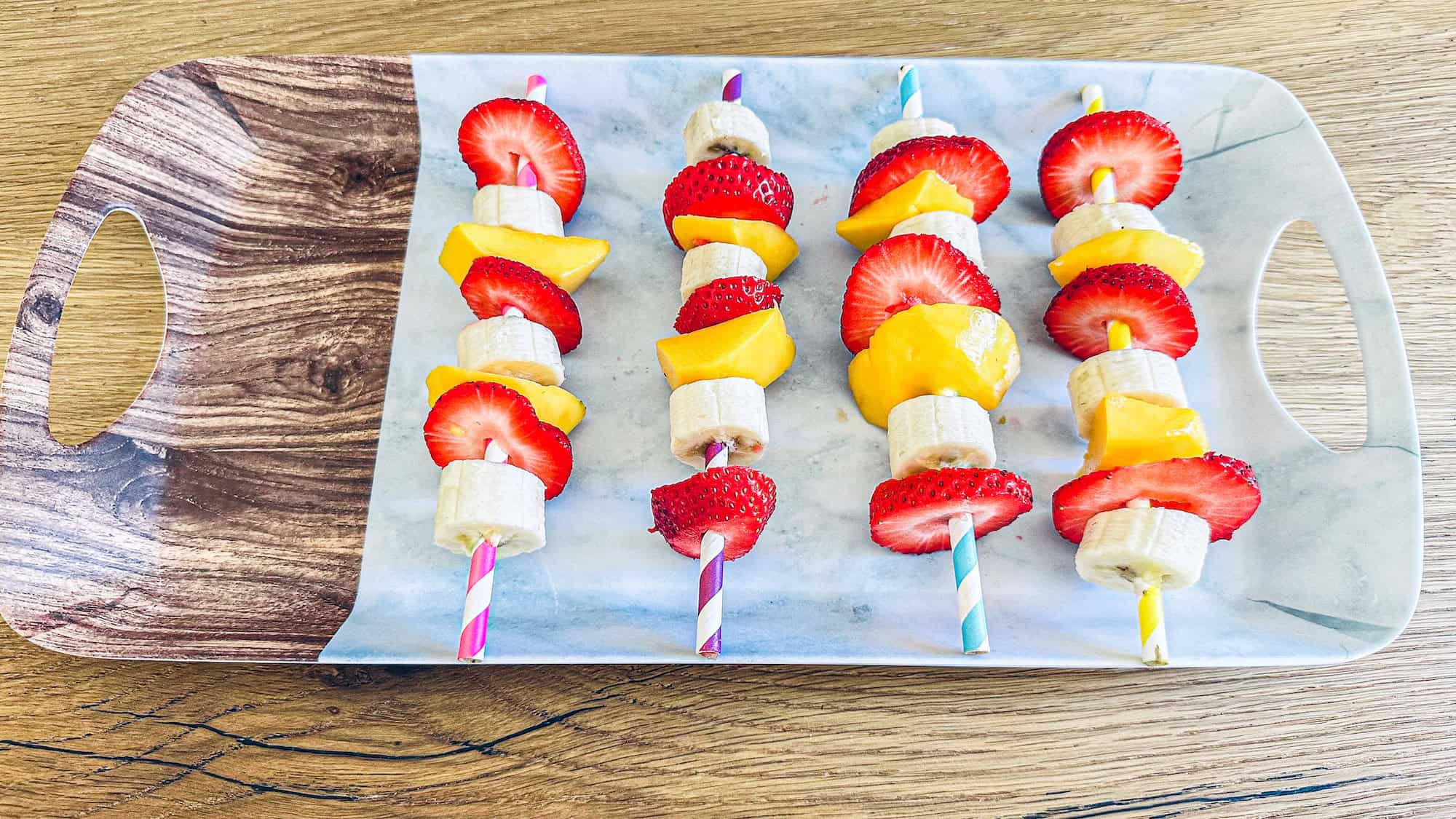 Fruit kabobs on plastic serving tray on wooden table.