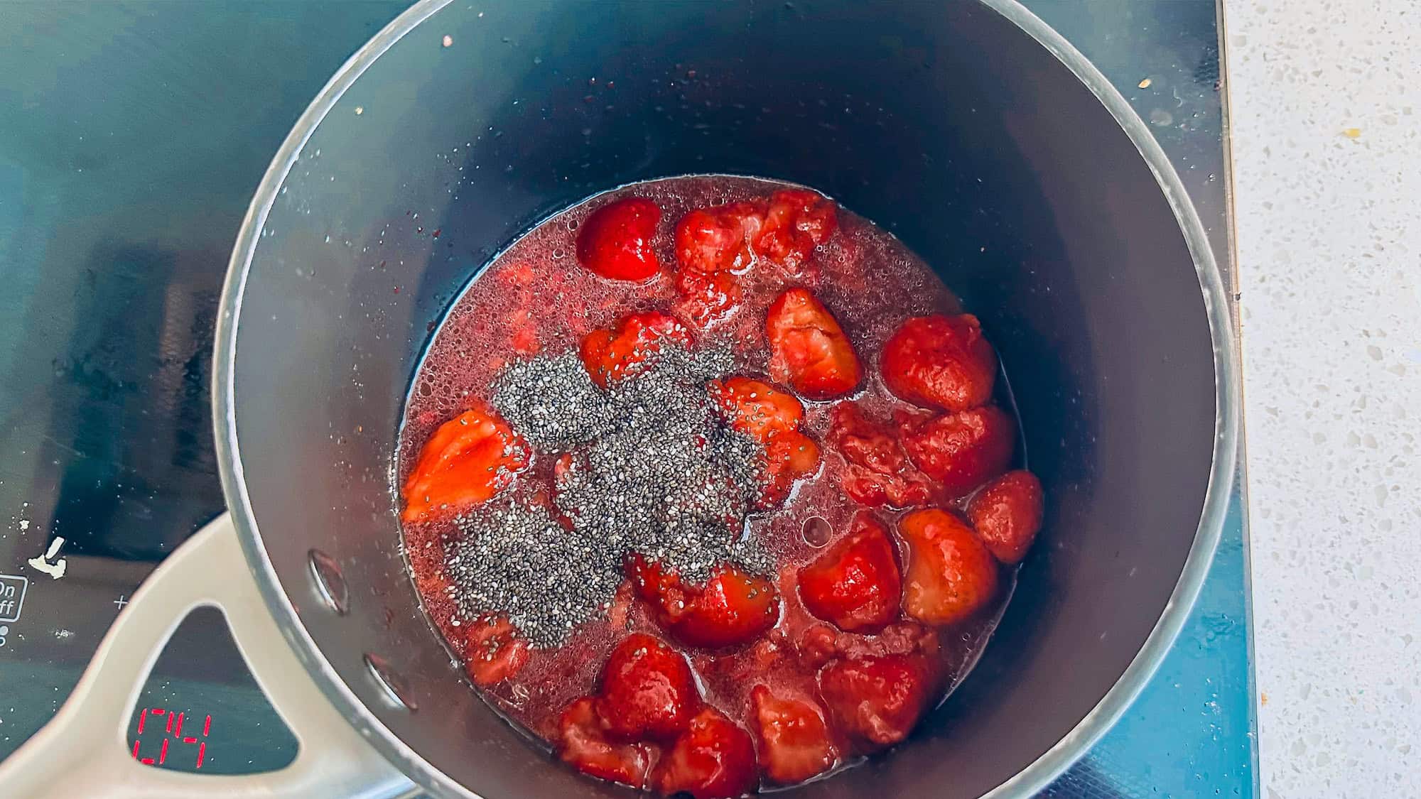 Step 2 of frozen yogurt protein bars. Chia seeds are added to strawberries in a pot on low heat.