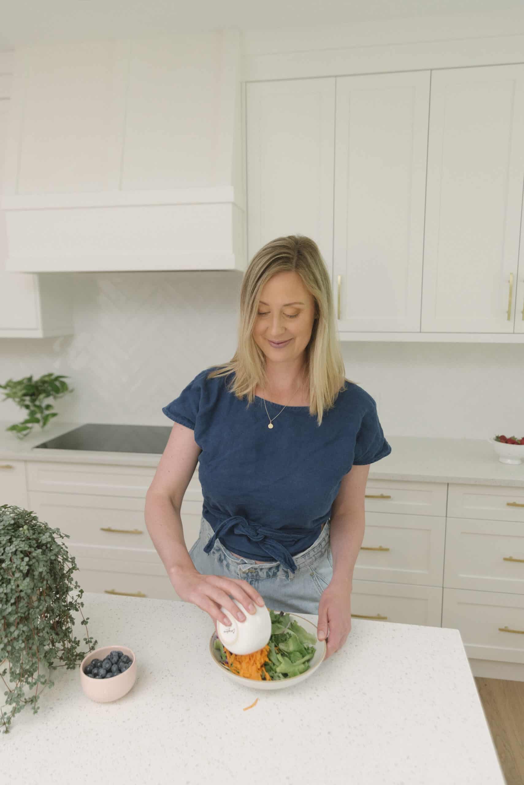 Dietitian in blue shirt adding carrots to a buddha bowl.