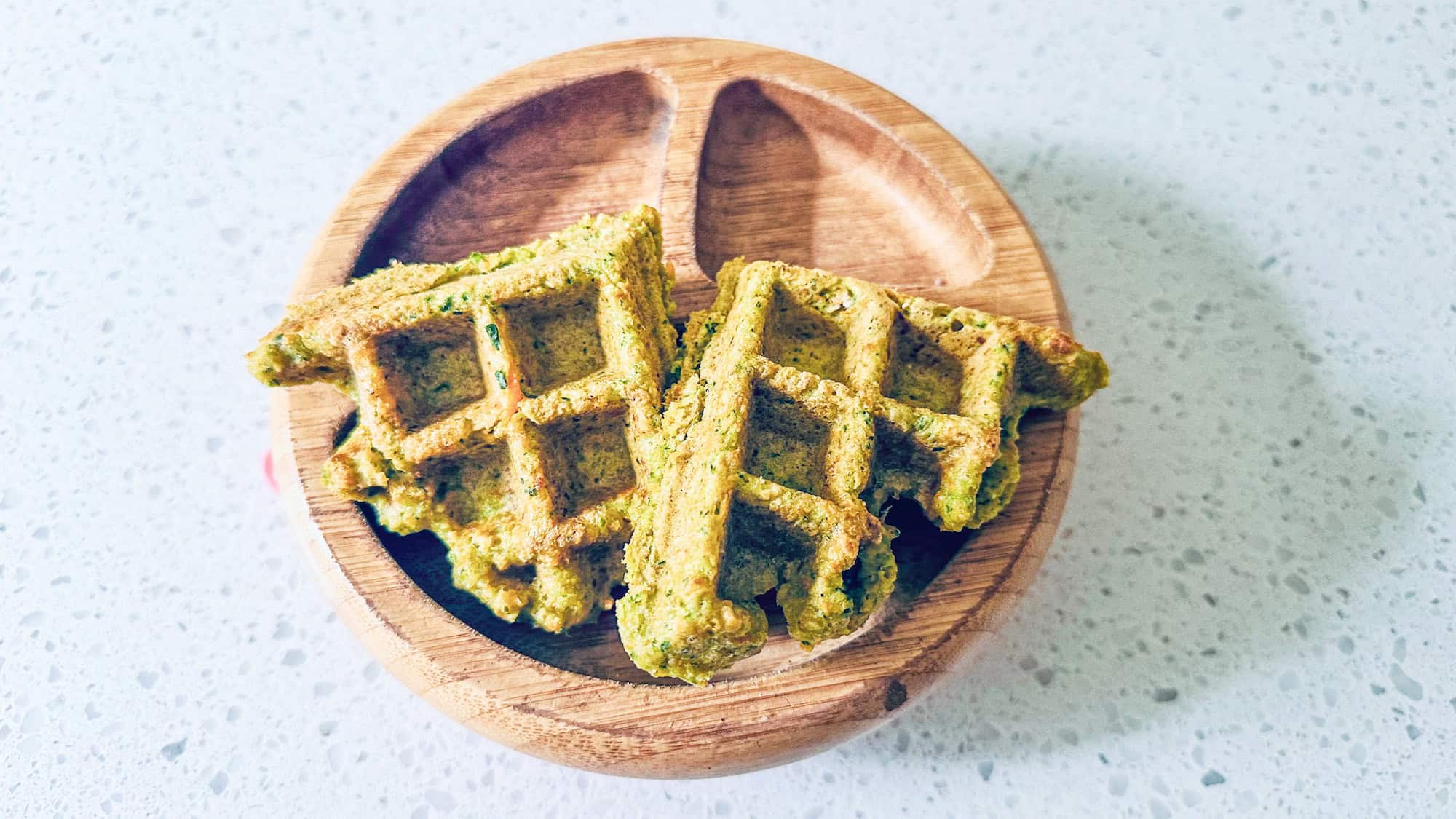 Savoury waffles in a wooden toddler bowl on white marble counter