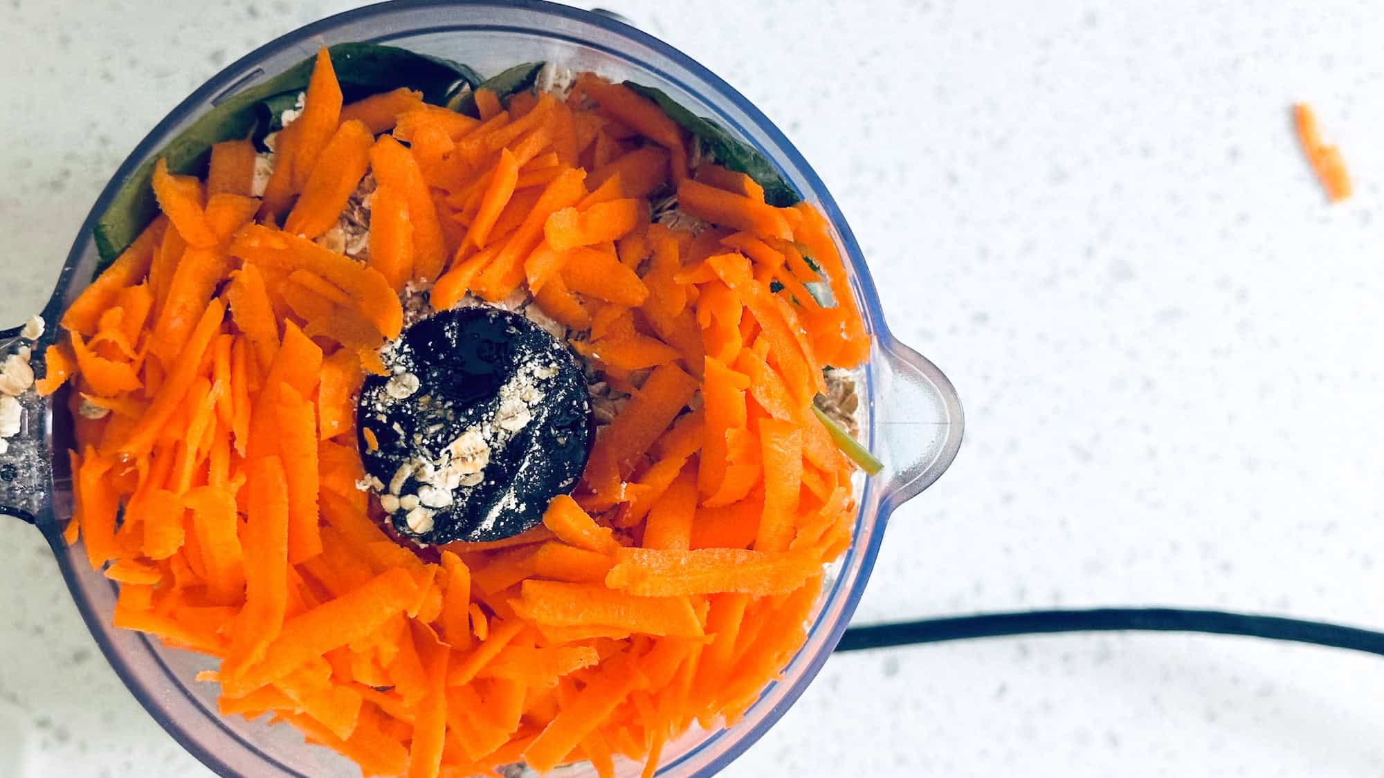 Image of grated carrot and waffle ingredients in a food processor