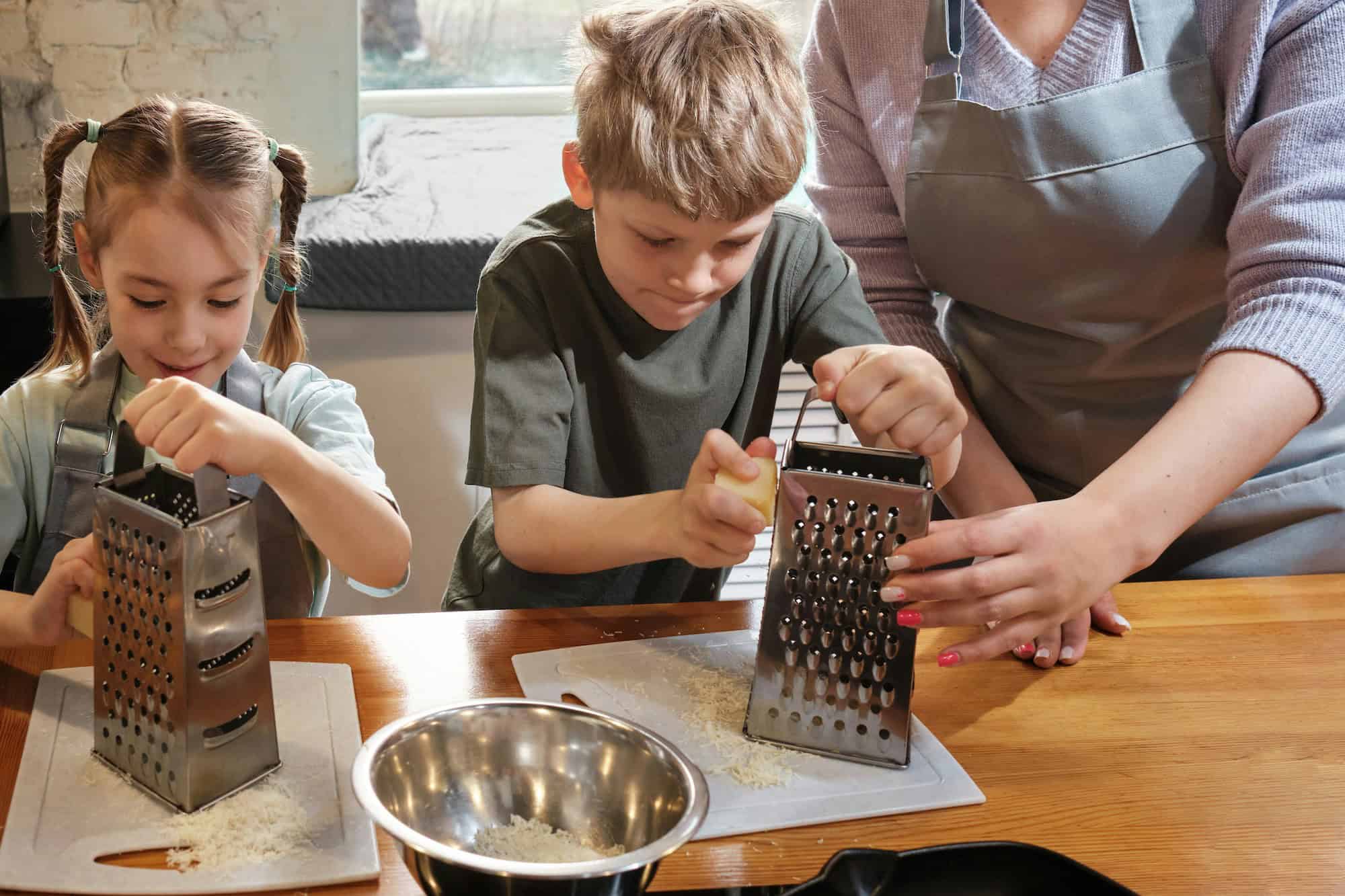 Mom and two young children grating cheese at kitchen counter.