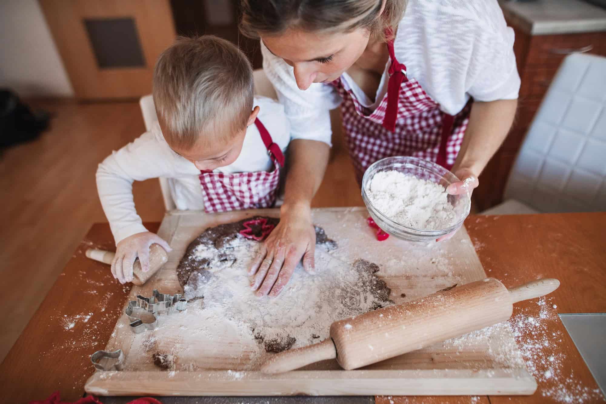 Mom and son patting flour onto dough wearing red checkered aprons.