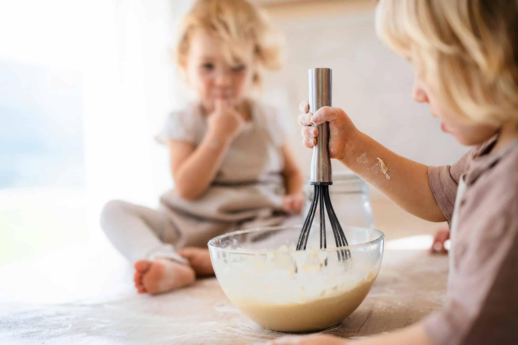 Image of two young children mixing batter in a bowl with other child sitting on counter.