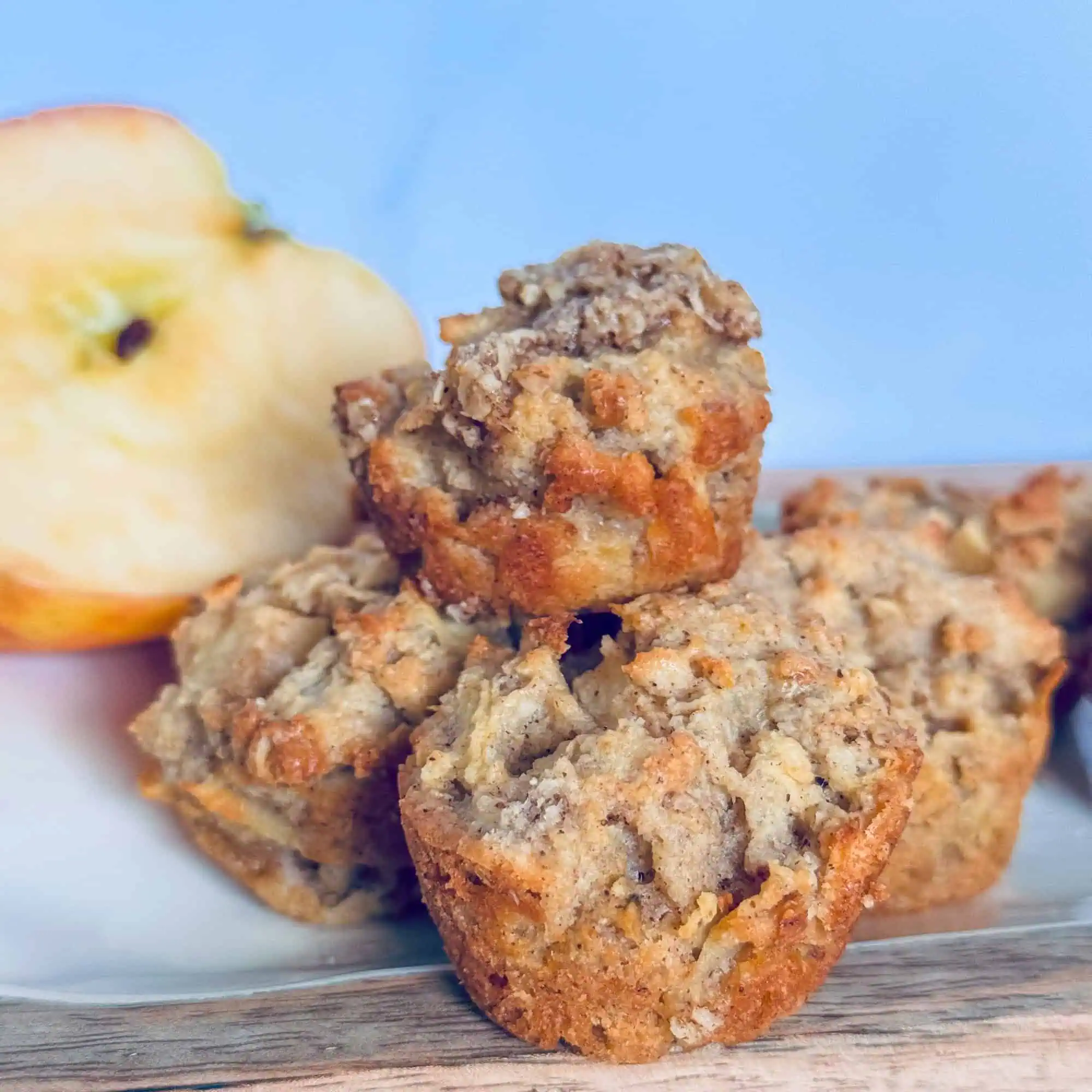 Apple and pear crumble muffins on wooden board with sliced apple in background.