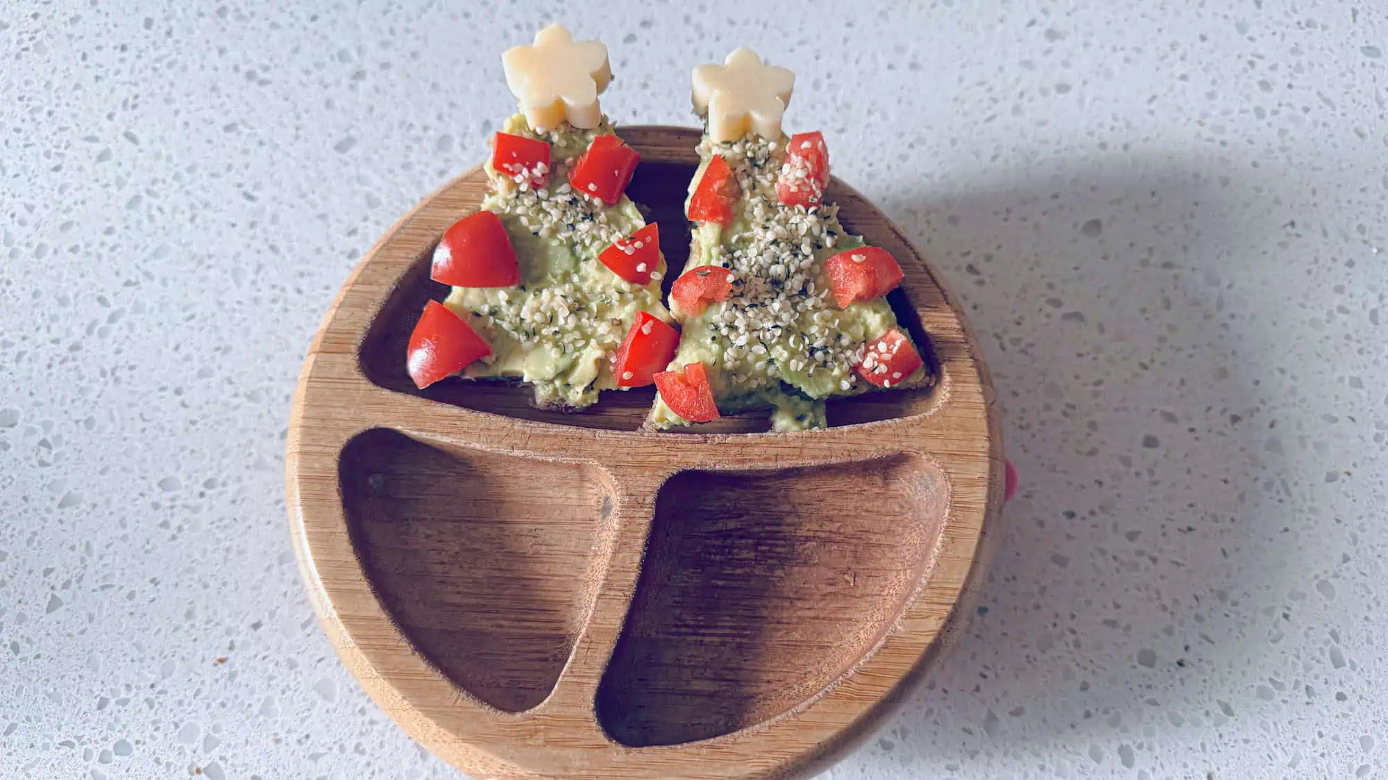 Avocado toast Christmas trees in a wooden toddler bowl on white marble background.