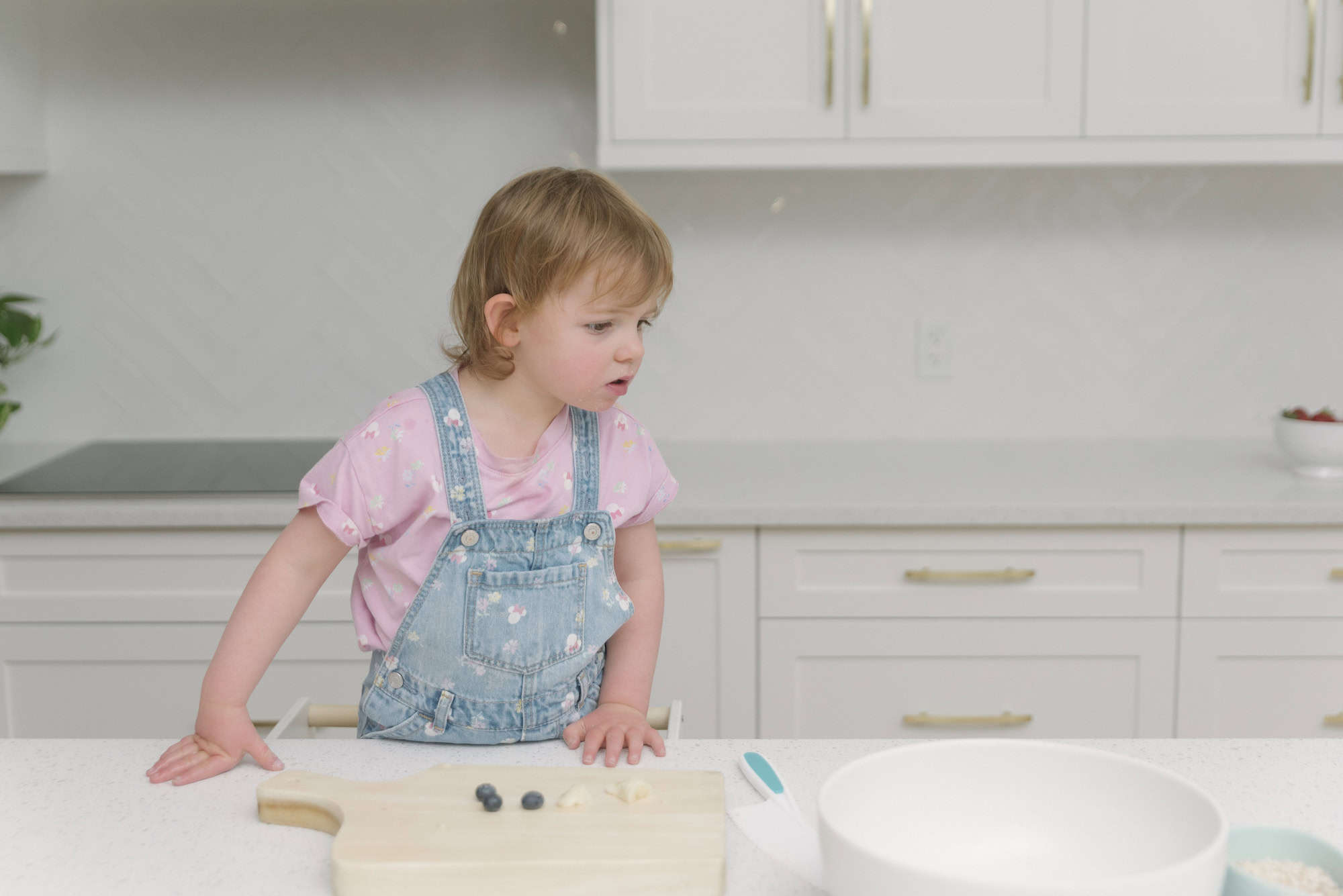 Child in denim overalls at safe cooking station in the kitchen.