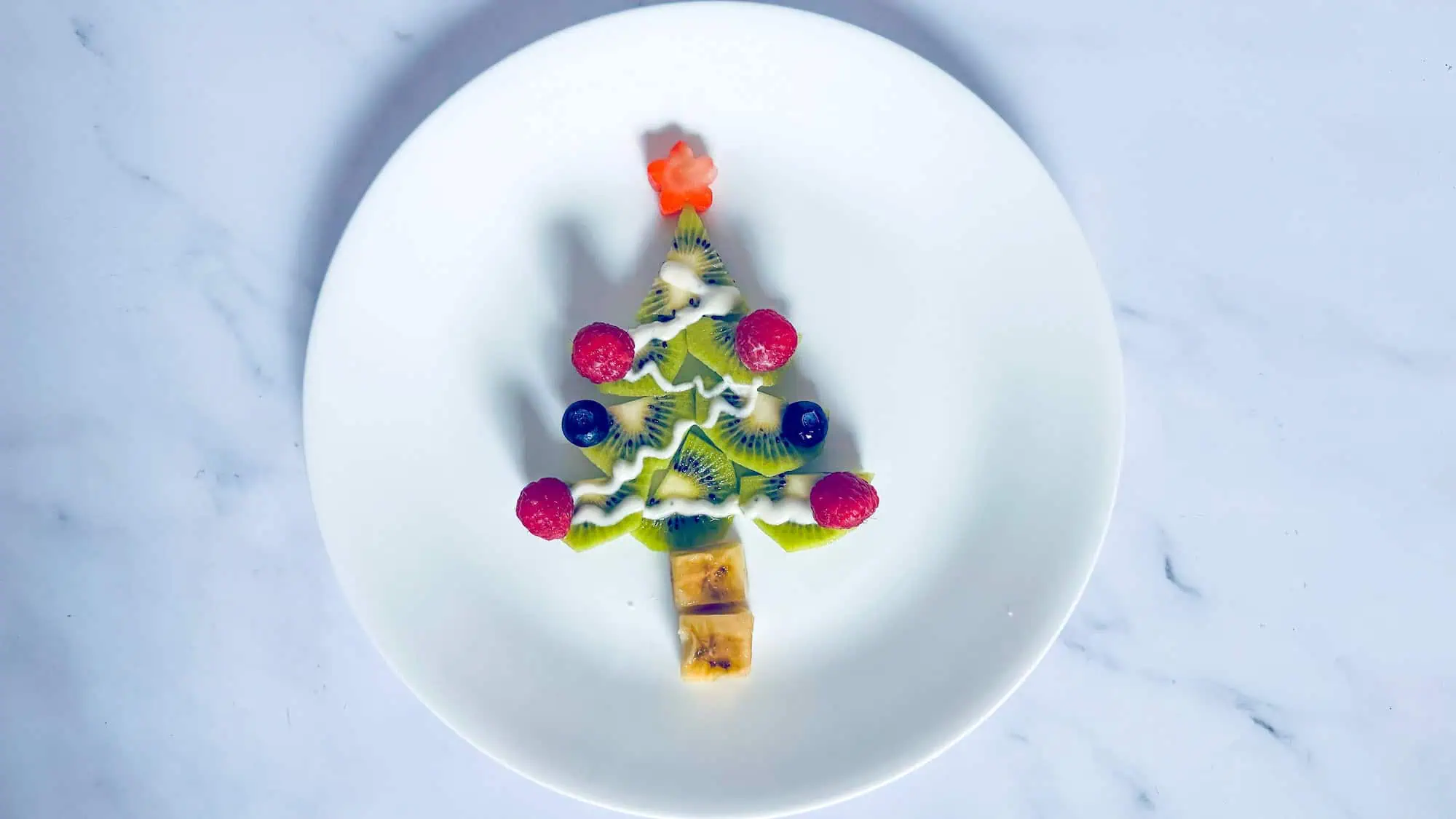 Fruit Christmas tree snack on white plate and white marble background.