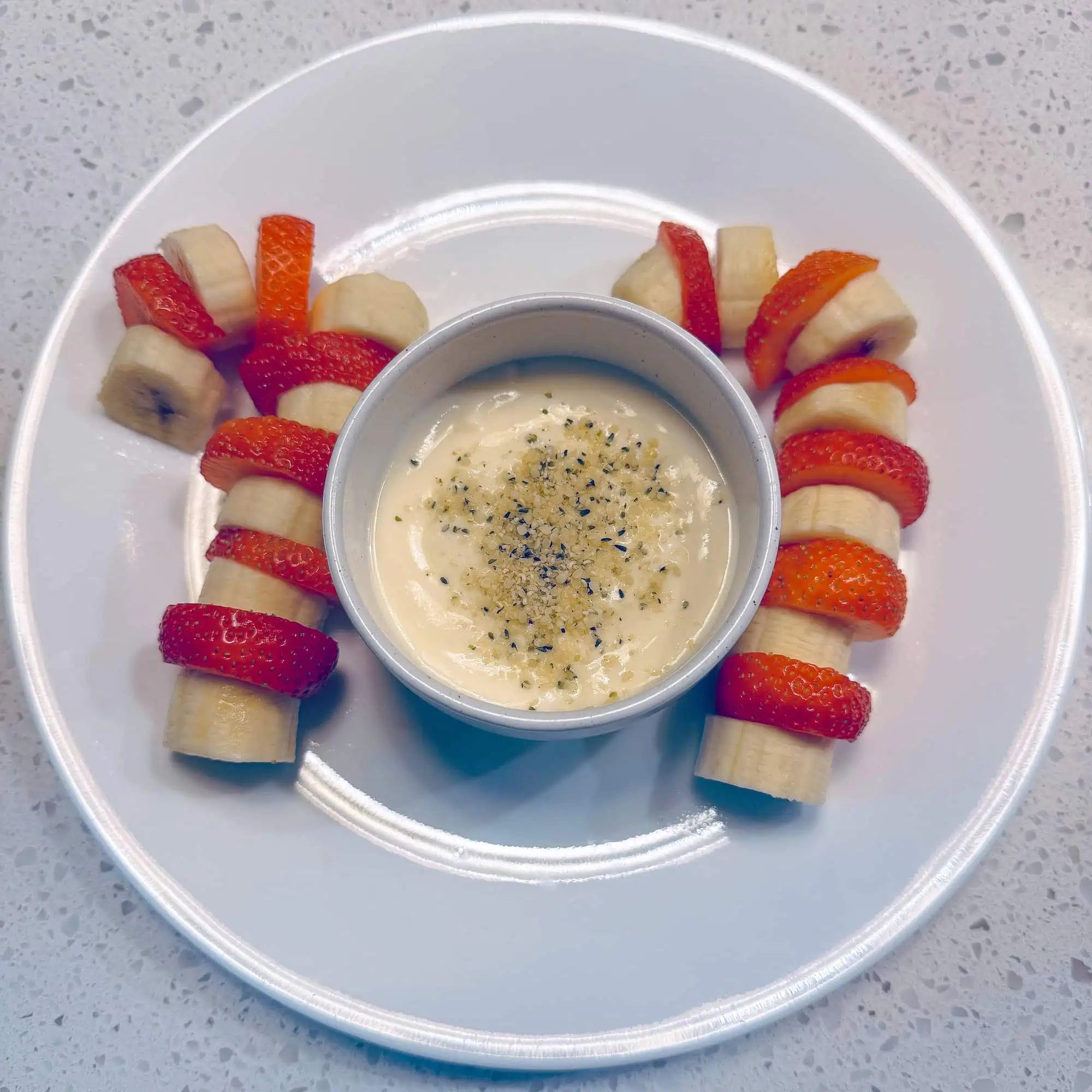 Strawberry and banana candy canes with yogurt dip on white plate.