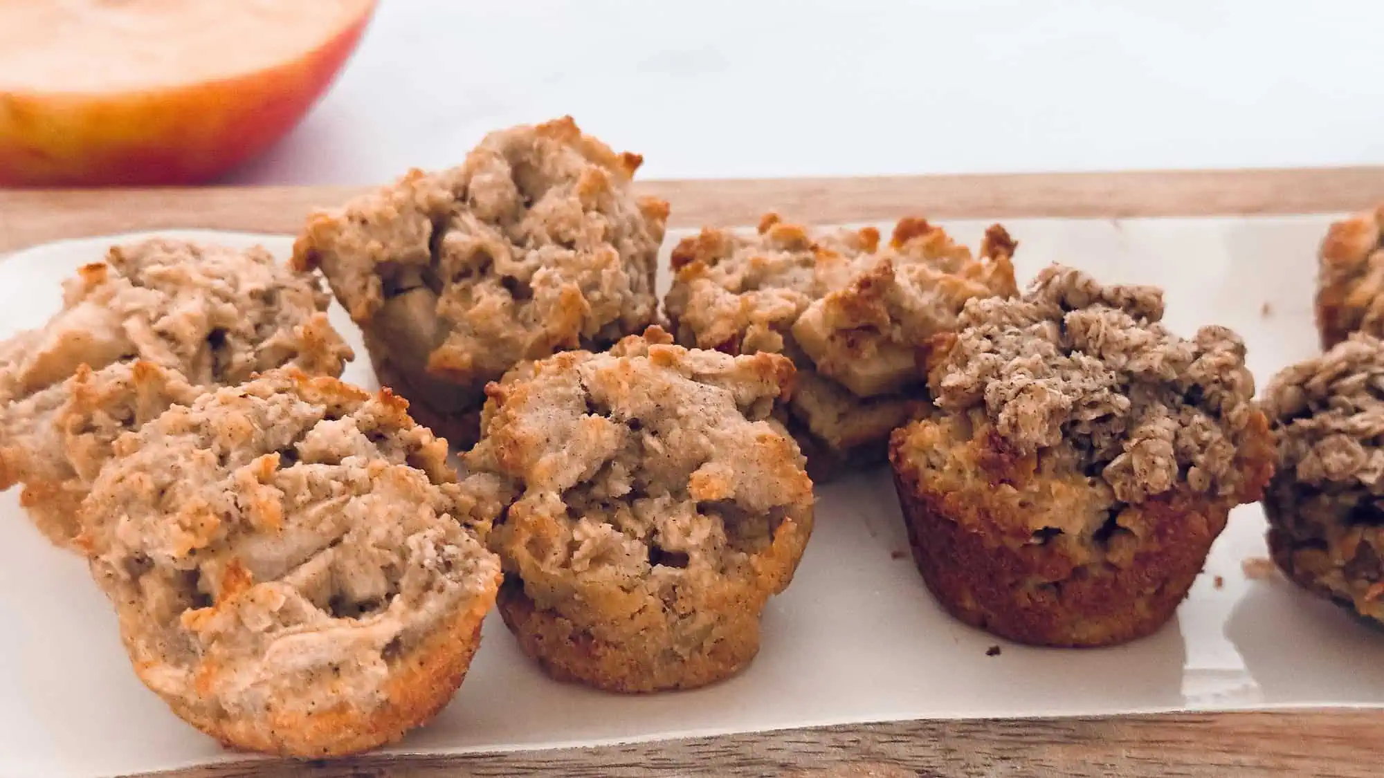 Image of apple and pear muffins on white plate with apple in background.