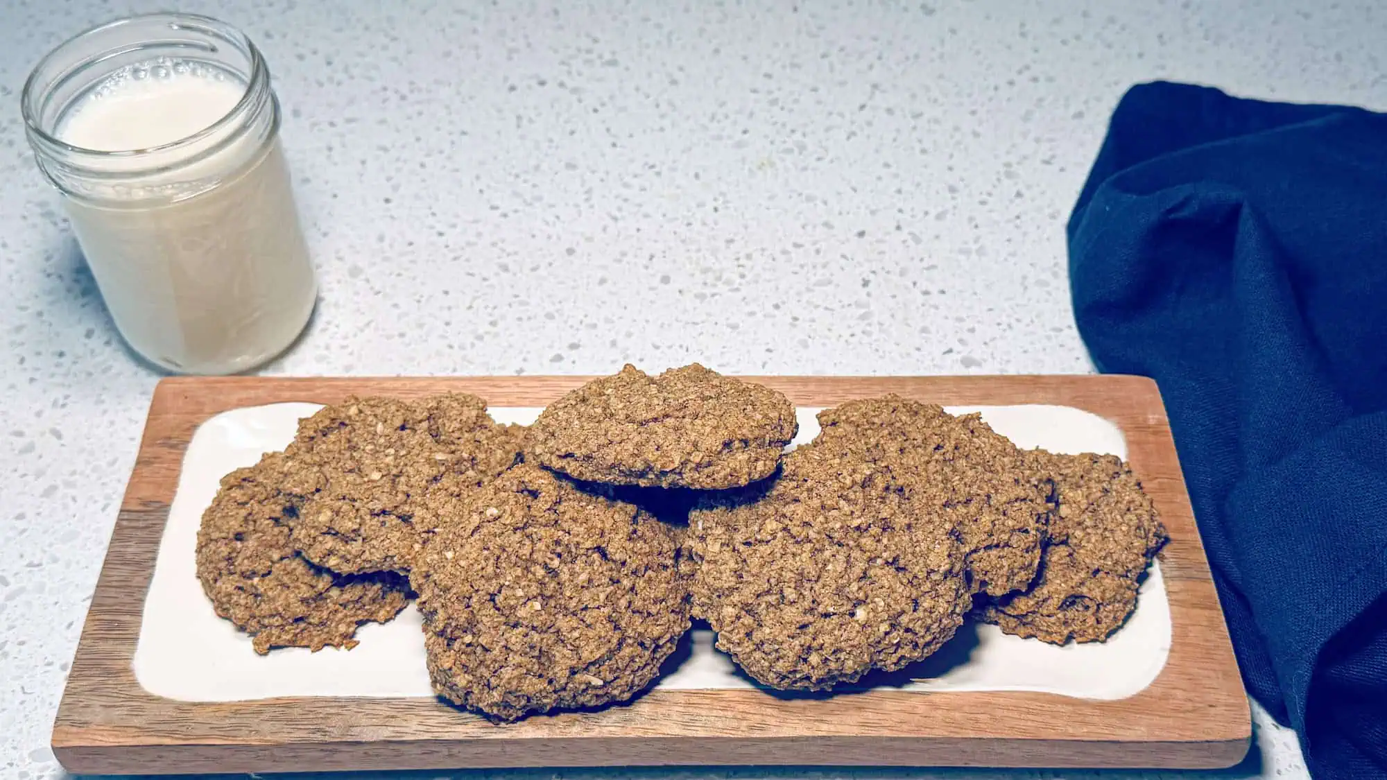 Vegan eggnog cookies on a wooden and white plate with a blue napkin and glass of milk.