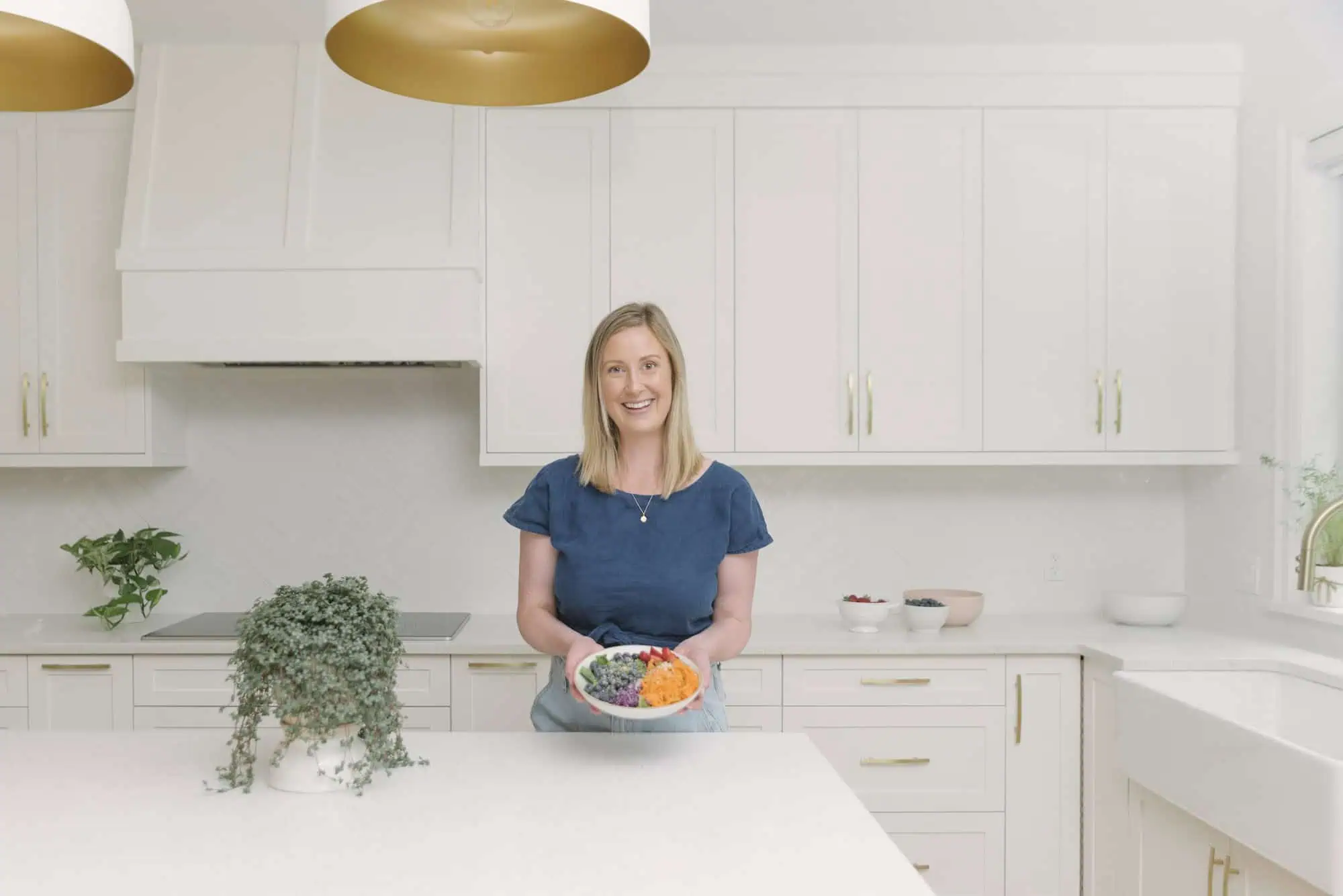 Dietitian in blue shirt holding a colourful bowl of food in a kitchen