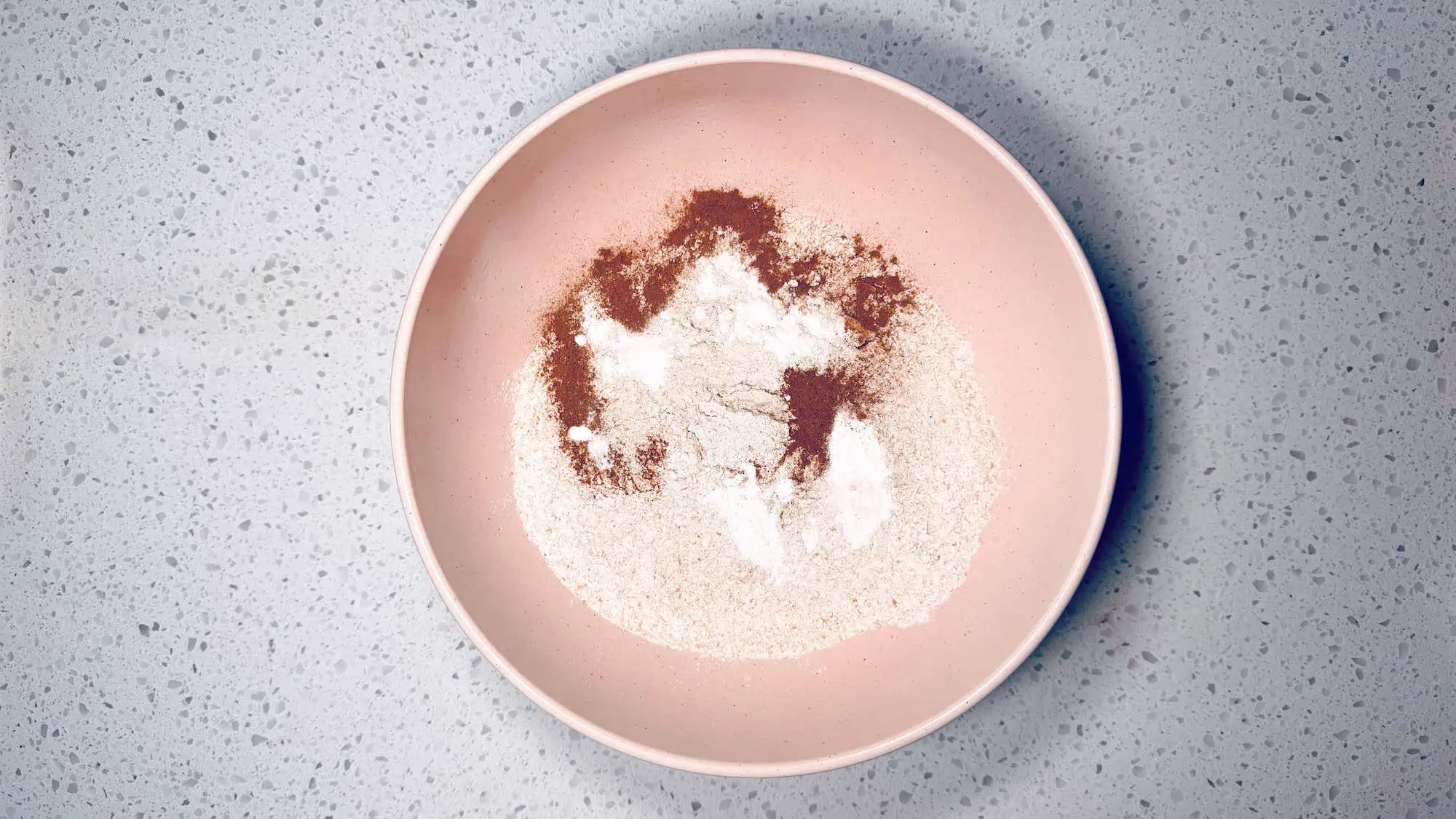 Step 1 of banana blackberry muffins, dry ingredients are added into a pink ceramic bowl.