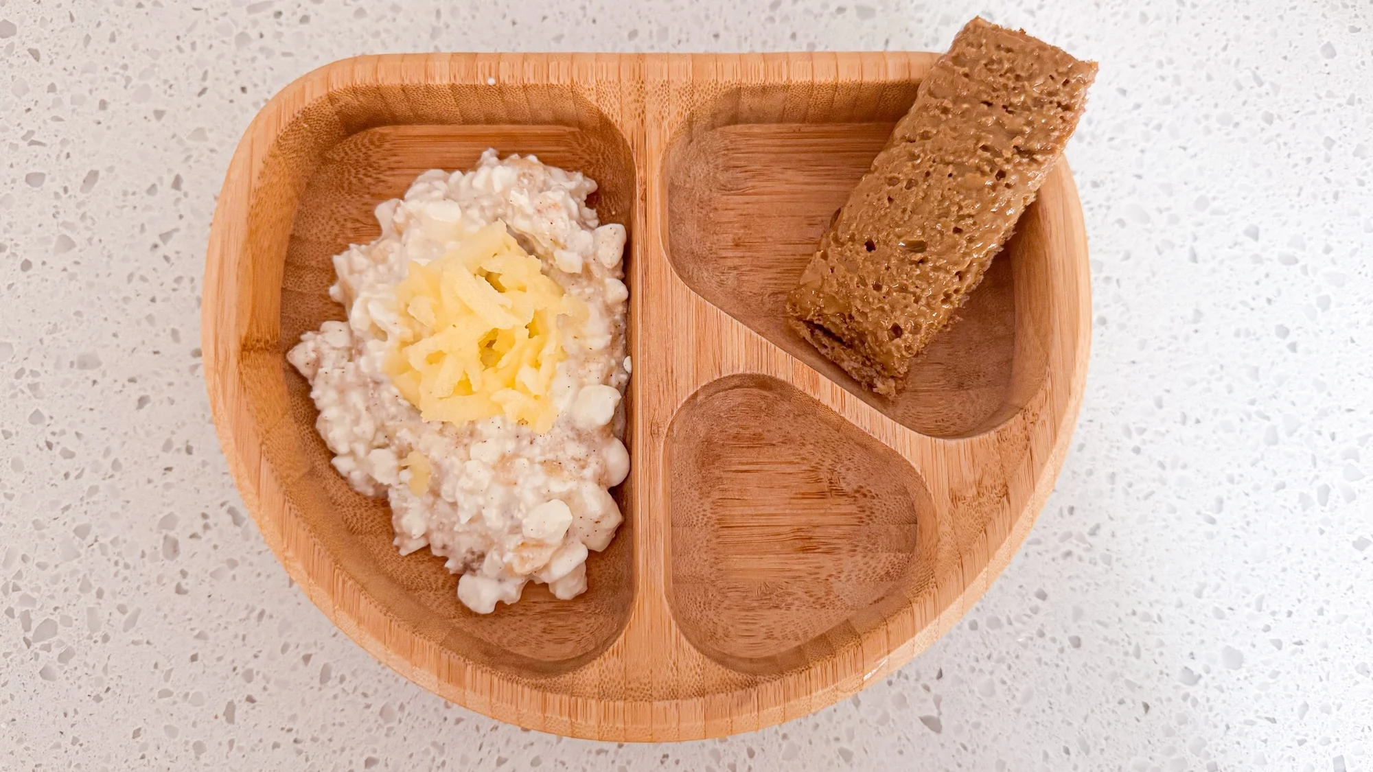 Baby-led weaning meal for 10 month baby includes cottage cheese with apple, toast strip in wooden baby plate.