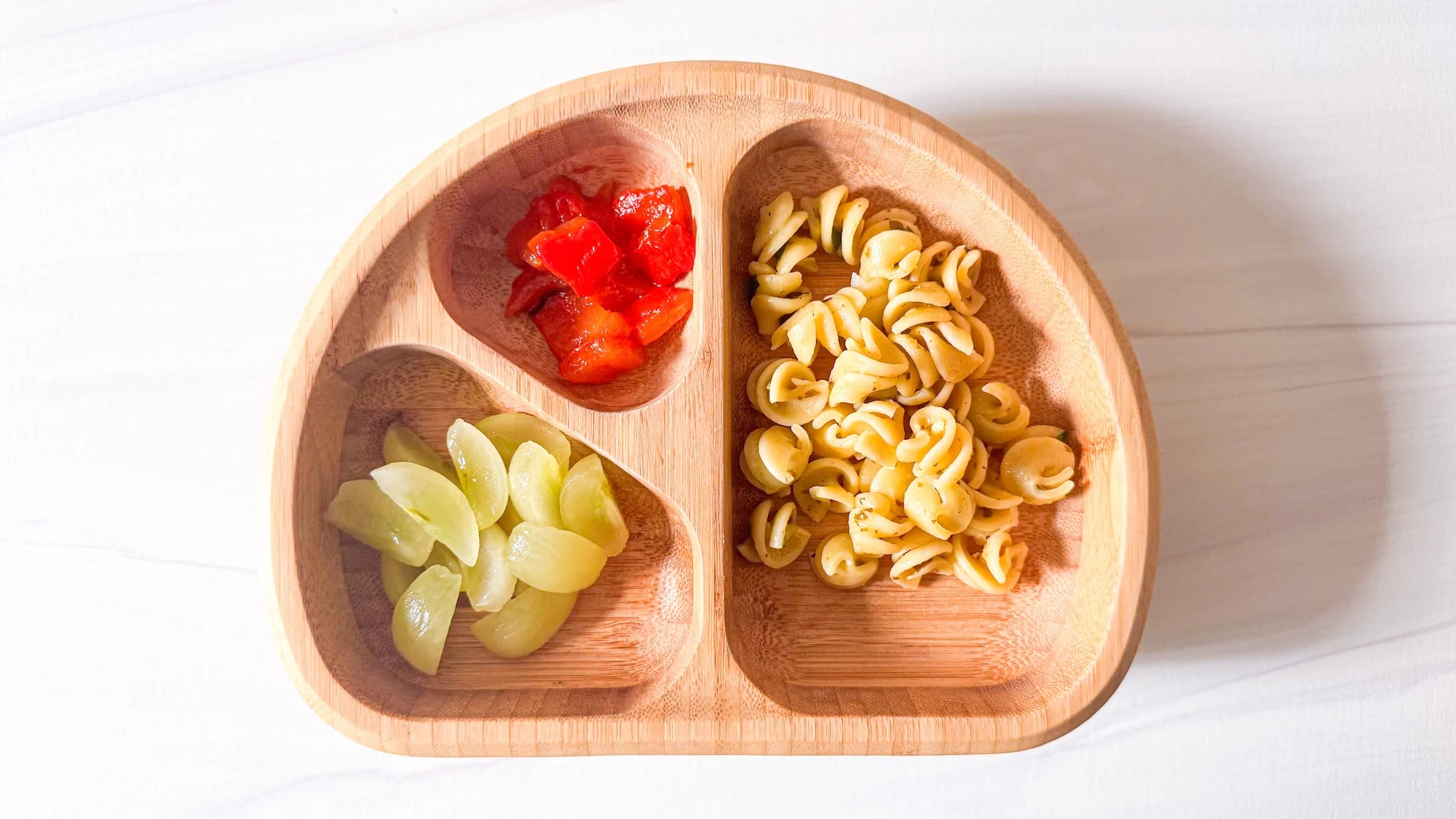 Baby-led weaning lunch idea with pasta, red pepper and grapes in wooden baby plate.