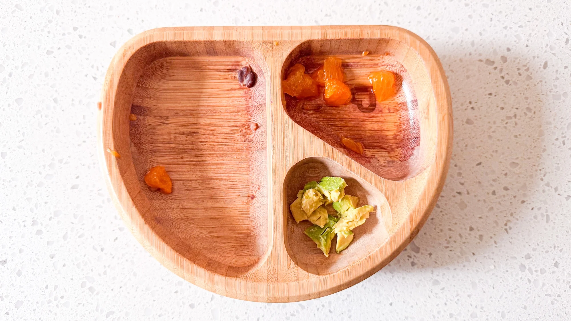 Leftovers of dinner on baby's plate. Small amount of avocado, and a few pieces of oranges.