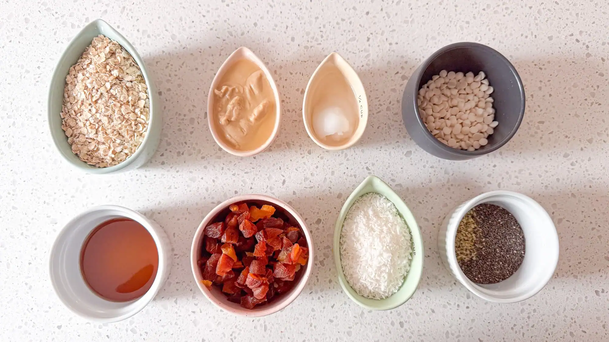 Ingredients for apricot and white chocolate energy balls on white marble counter top.