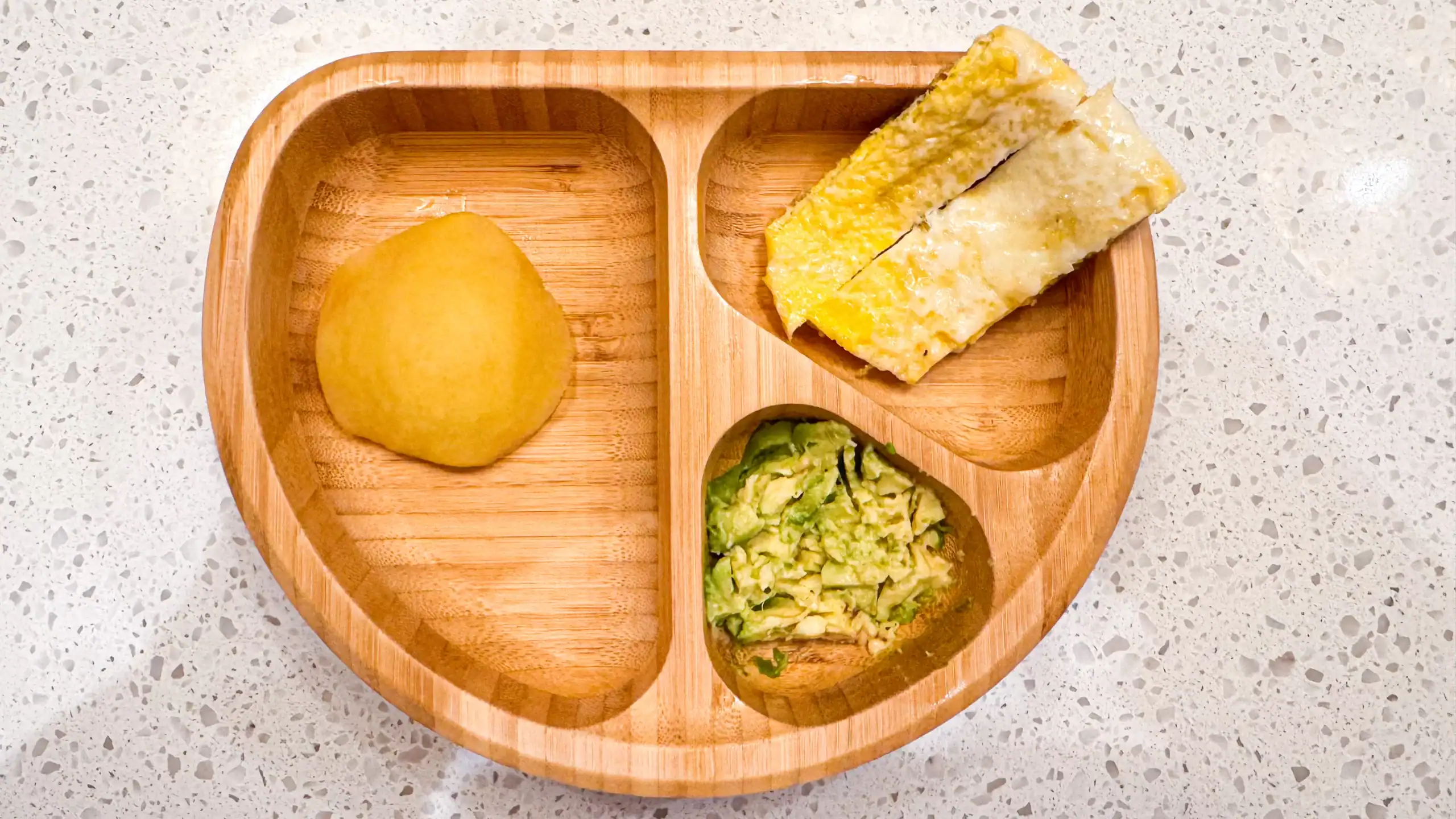 Omelette strips, half steamed apple, avocado in wooden baby bowl.