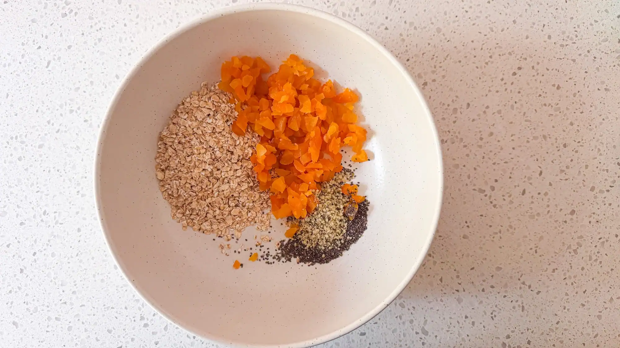 Step 2 for energy balls. Dry ingredients are added to white bowl.