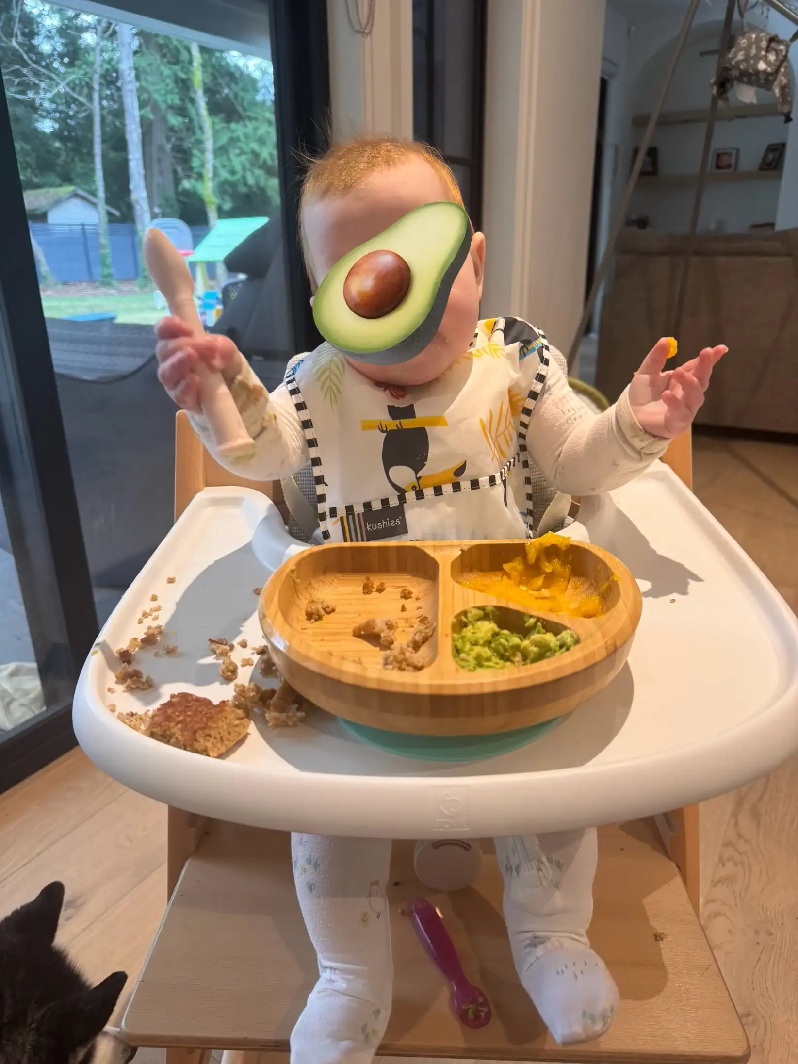 Baby sitting at a high chair doing baby led weaning eating avocado and pancake.