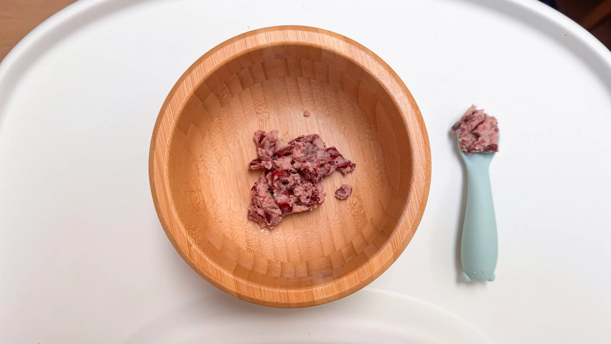Mashed beans in a baby bowl on a white tray on a baby's high chair. Blue baby spoon loaded with some mashed beans.
