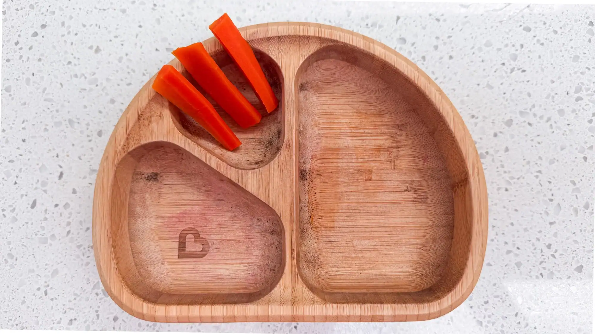 Steamed carrots in wooden baby bowl on counter.