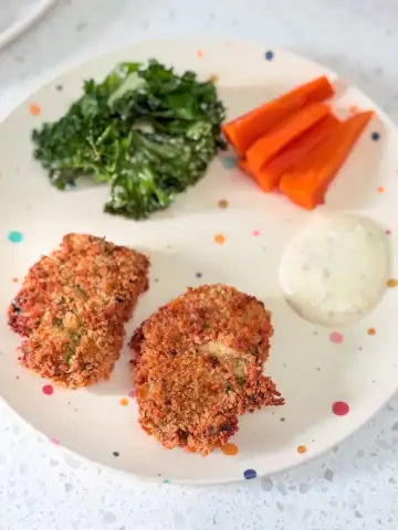 air fryer chicken nuggets on polka dot toddler plate served with dip, carrots and kale chips.