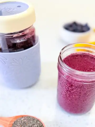 Blueberry prune constipation smoothie for toddlers in a small glass with toddler cup in background.